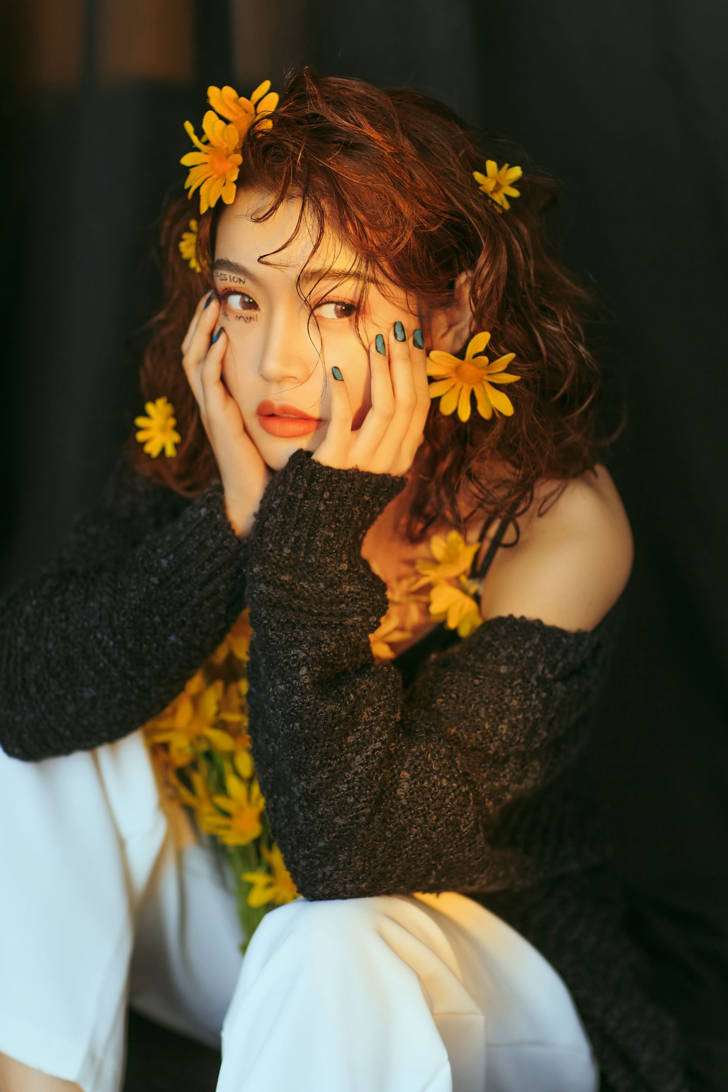 Artistic portrait with yellow daisies adorning dark curly hair against a black background with white accents.