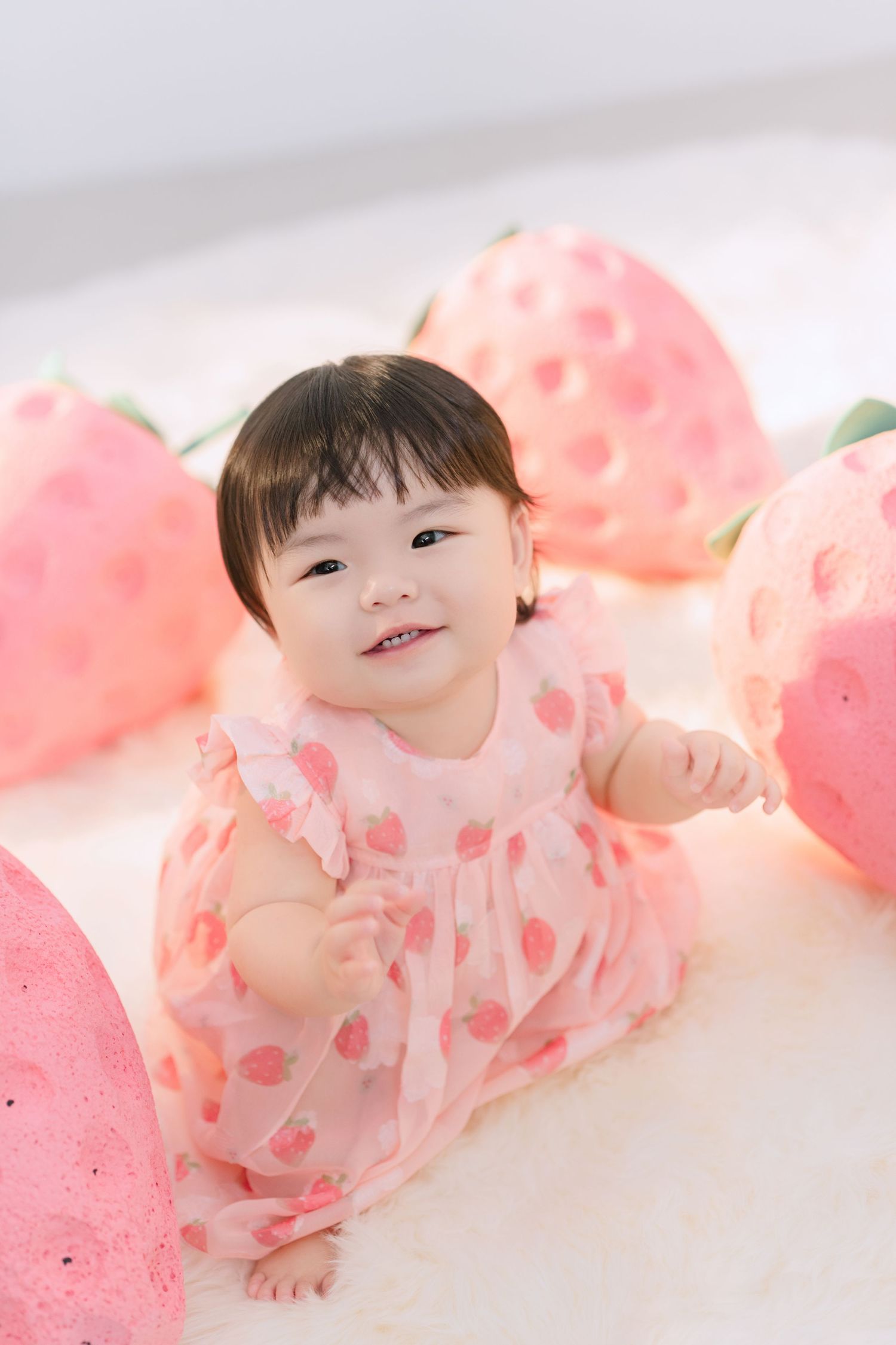 Baby in pink floral outfit lying on white backdrop with soft pink decorative elements.