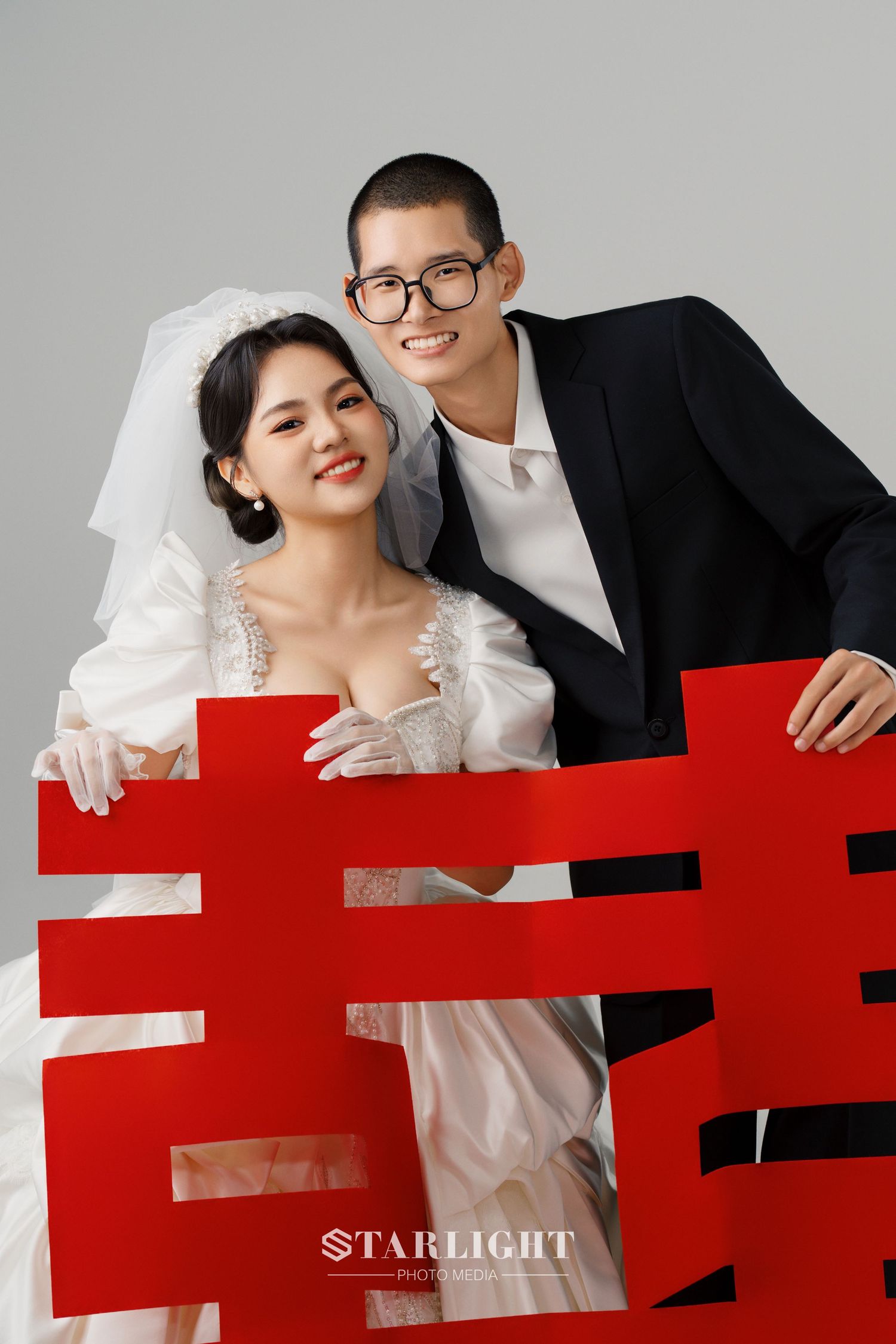 Wedding couple poses playfully behind a red geometric element in a modern studio portrait series.