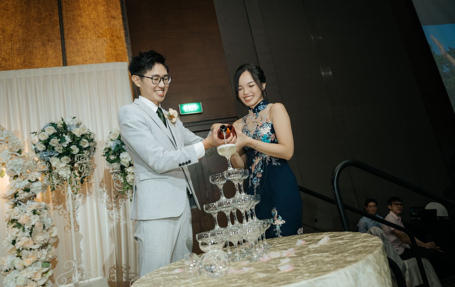 Wedding reception guests celebrate at elegantly decorated tables with floral centerpieces and stemware.