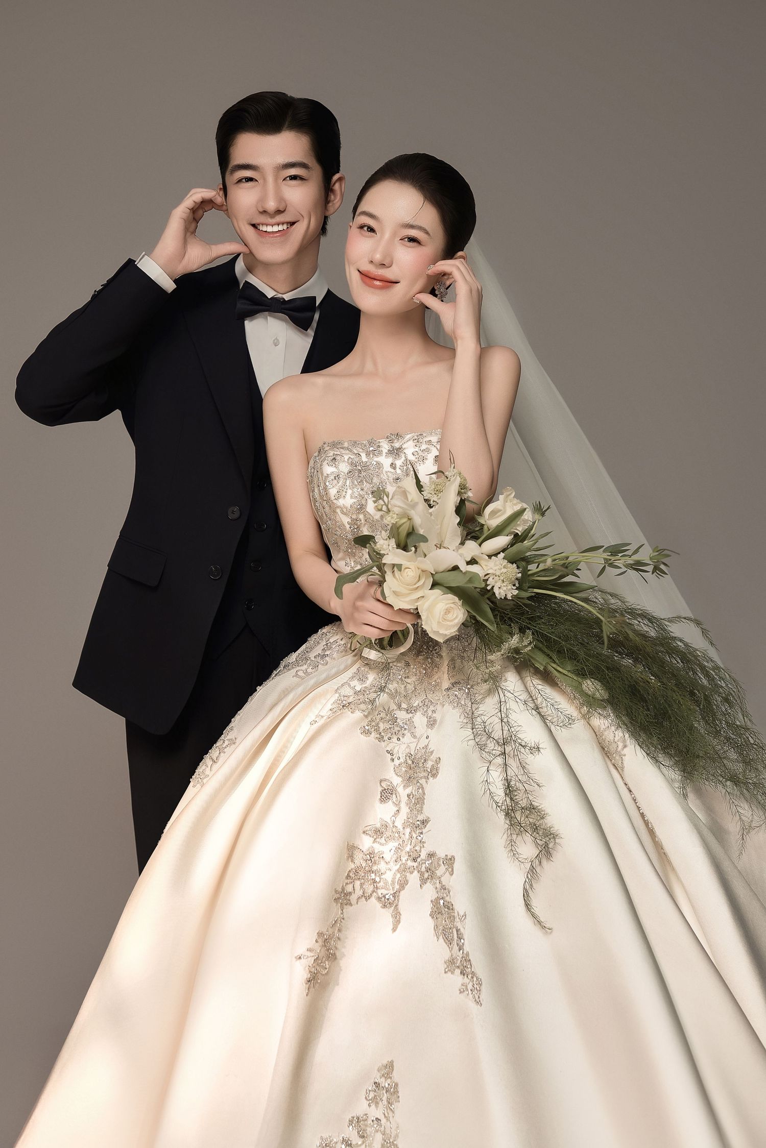 Elegant couple in wedding attire, groom in black tuxedo and bride in embellished ballgown holding floral bouquet.
