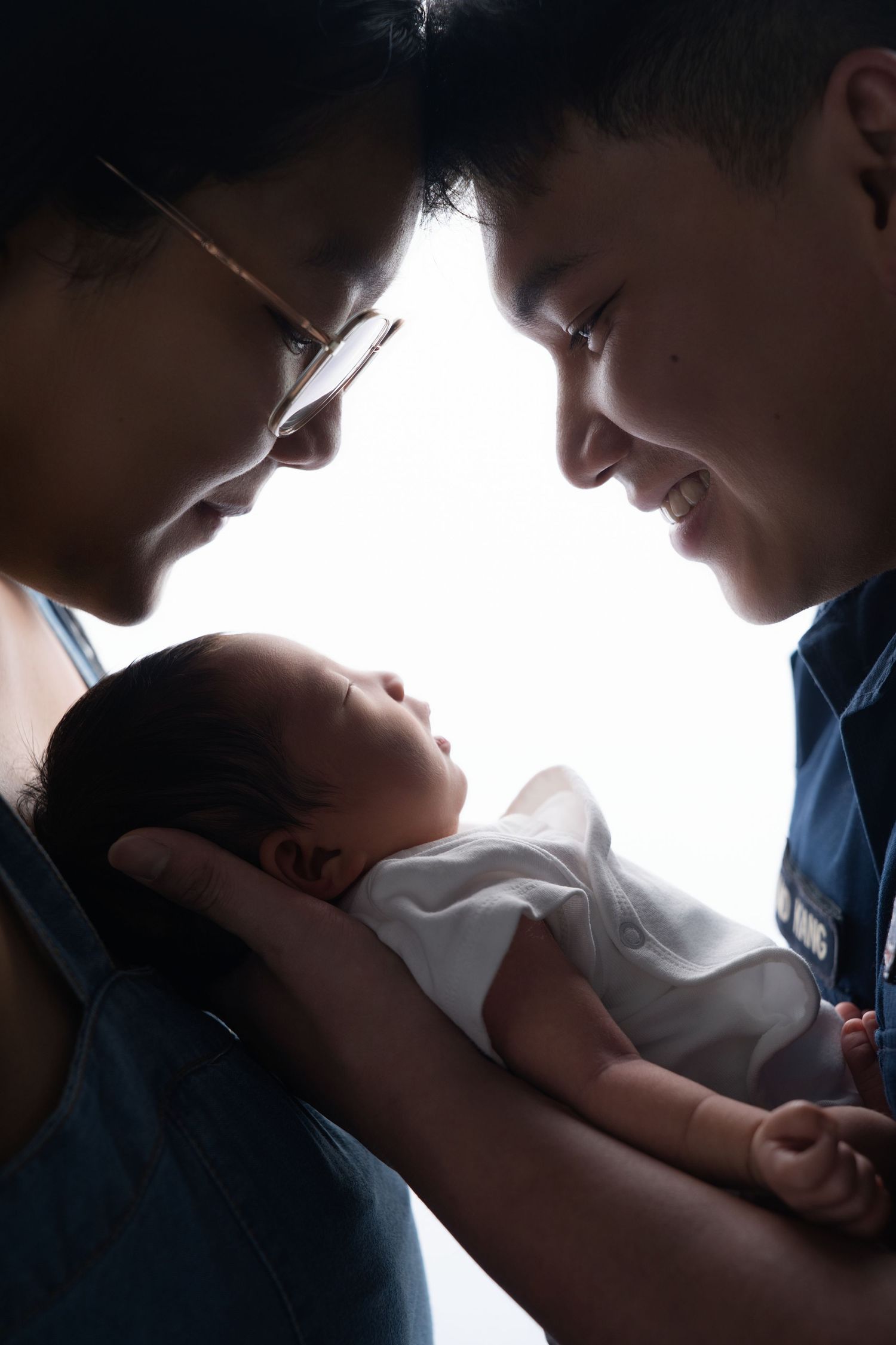 Two parents lovingly gaze at their newborn baby, cradling the infant gently in a tender family portrait.