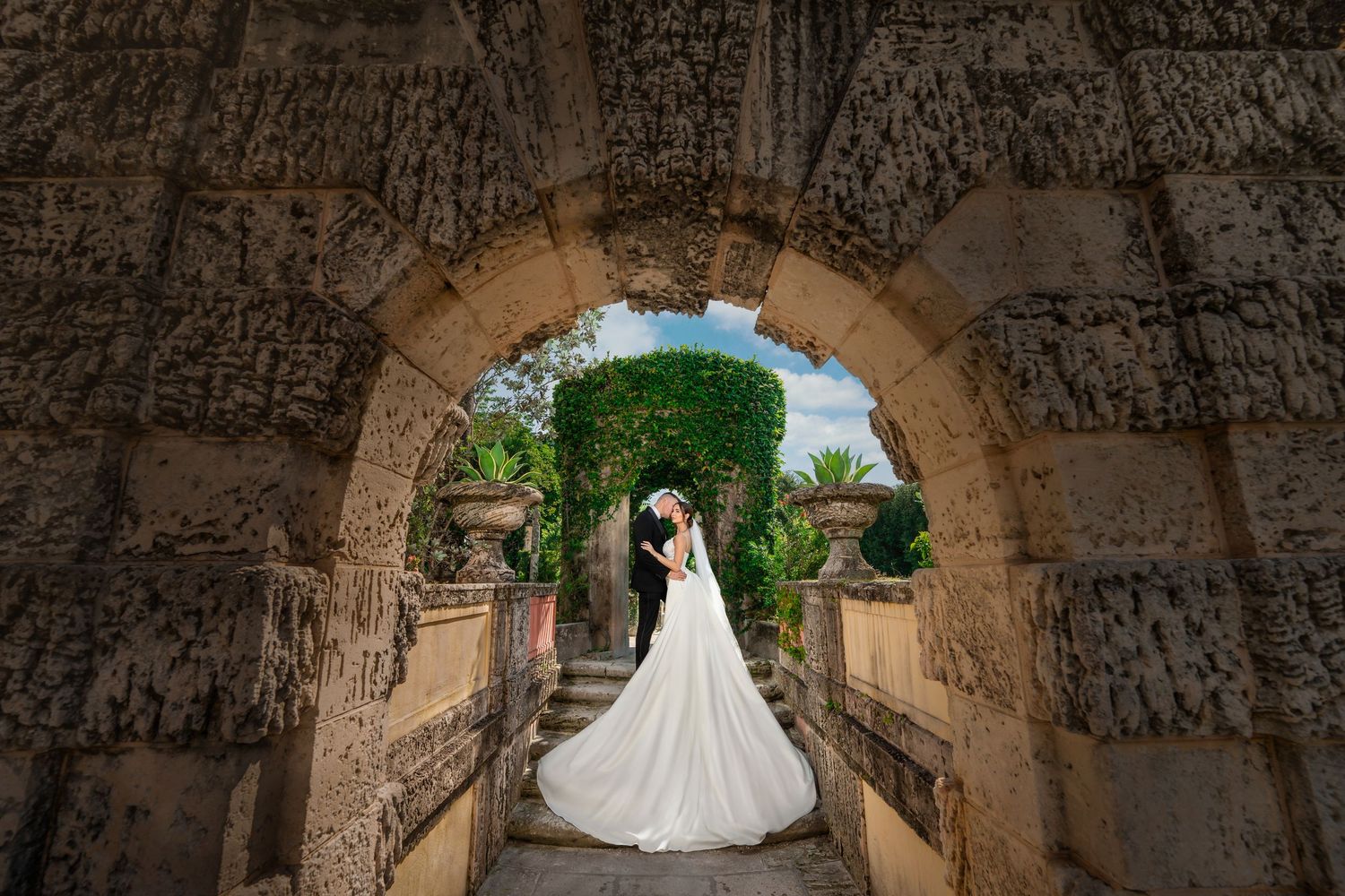 Bride posing under an ancient stone arch at Vizcaya in Miami—cathedral-length gown captured in an elegant outdoor portrait.