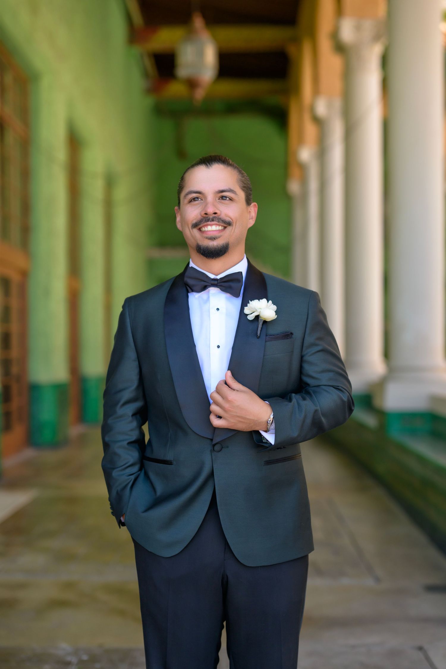 Groom poses confidently in a sharp tuxedo under elegant arches.