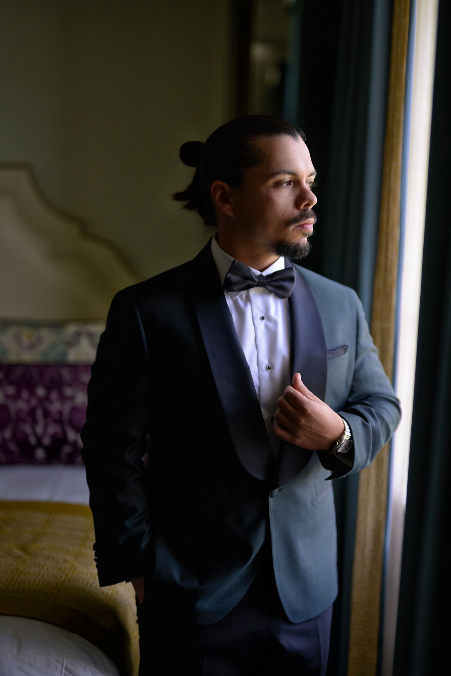 Groom adjusts his jacket by the window, calm before the ceremony.