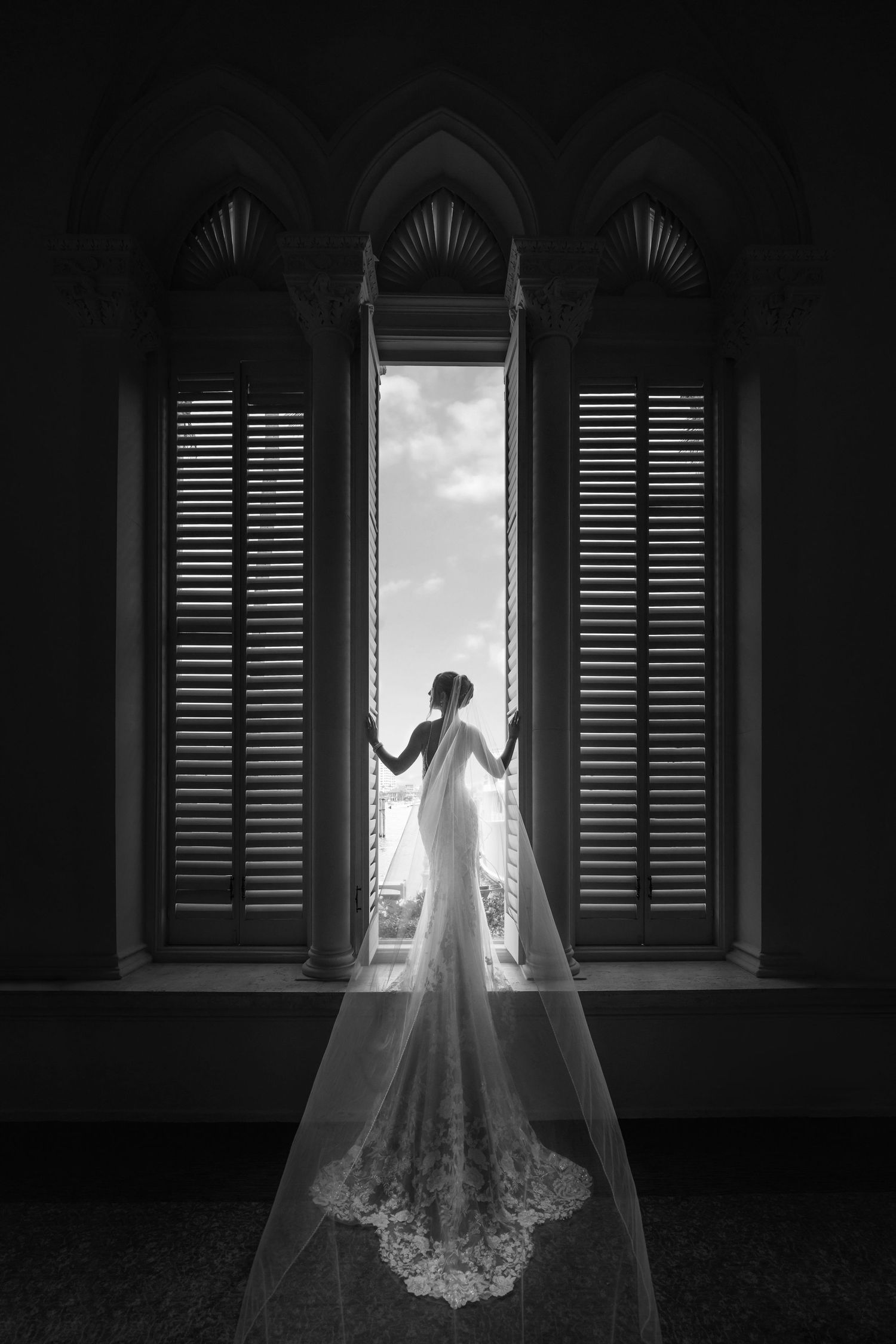 Black and white bridal portrait in front of gothic arched windows—timeless, editorial wedding style.