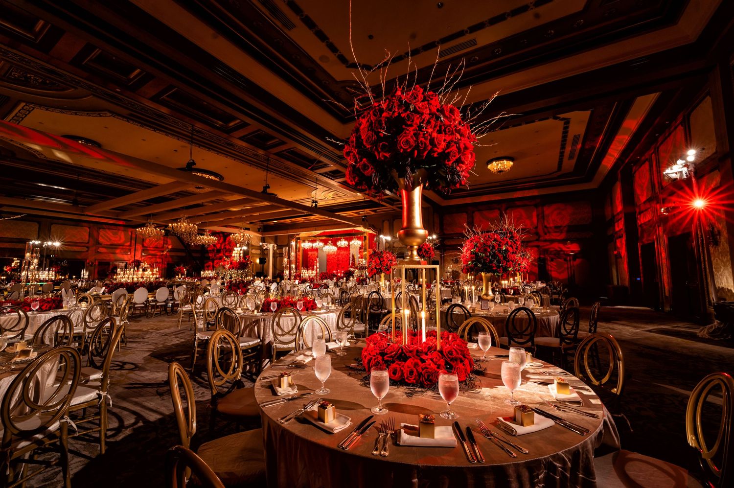 Luxury wedding reception with dramatic red floral centerpieces and candlelit tables in an elegant ballroom.