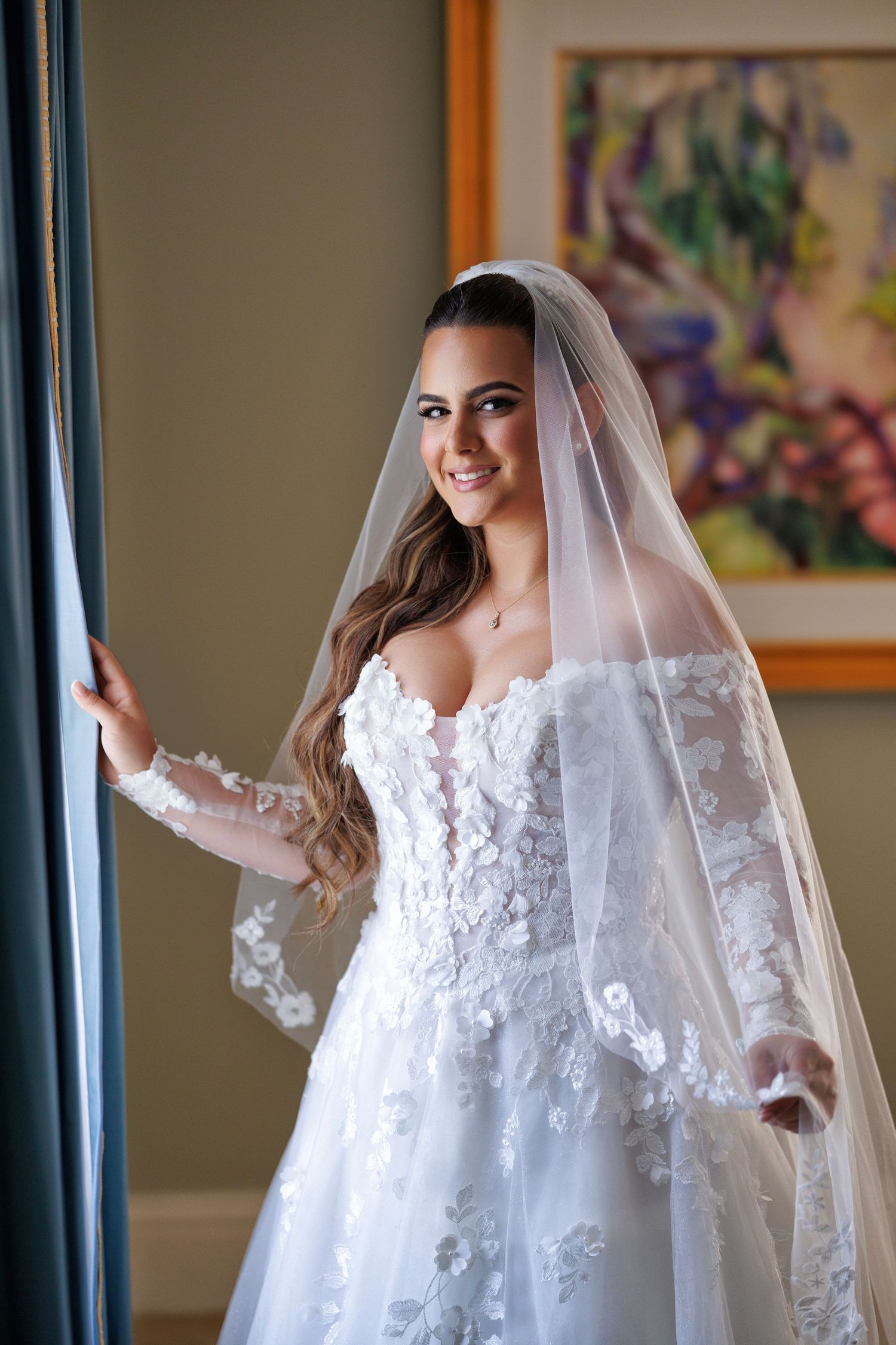 Bride gazing out a window in a lace gown—elegant bridal portrait with natural light.