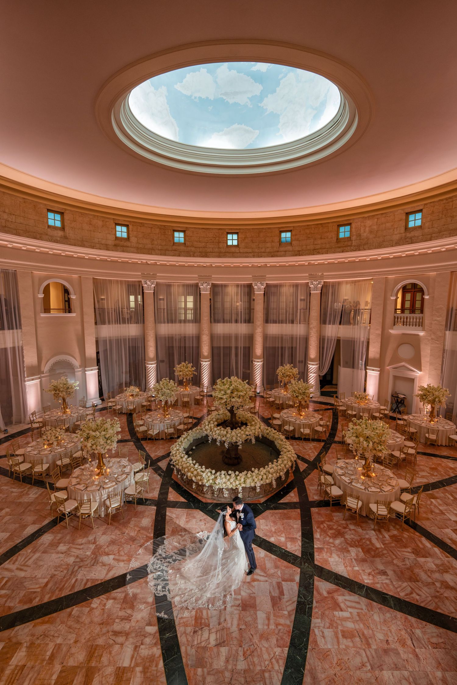 Grand ballroom set for a wedding reception—round tables, elegant décor, and a domed ceiling centerpiece.