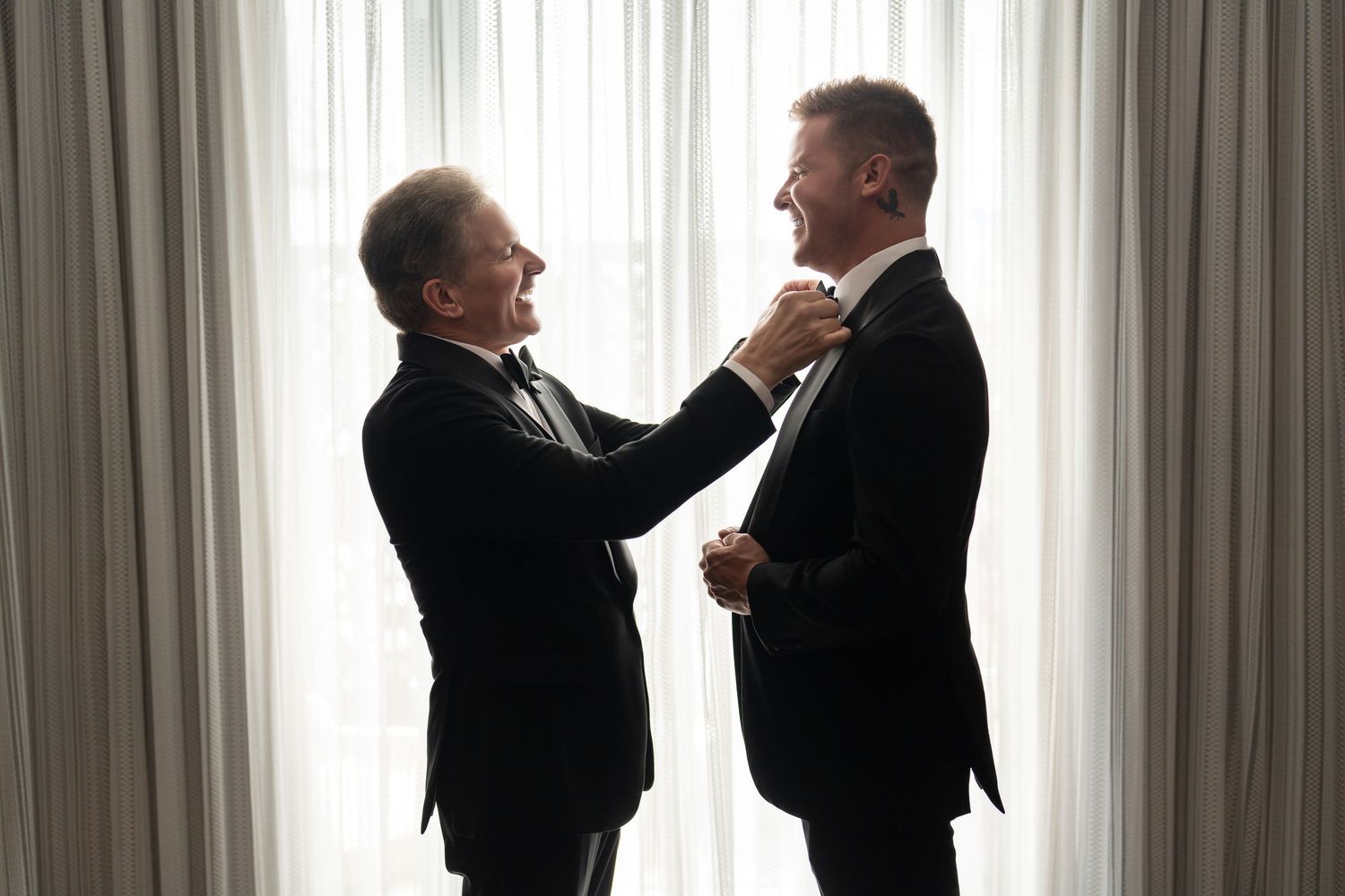 Groom getting ready with his father—classic wedding day moment with natural window light.