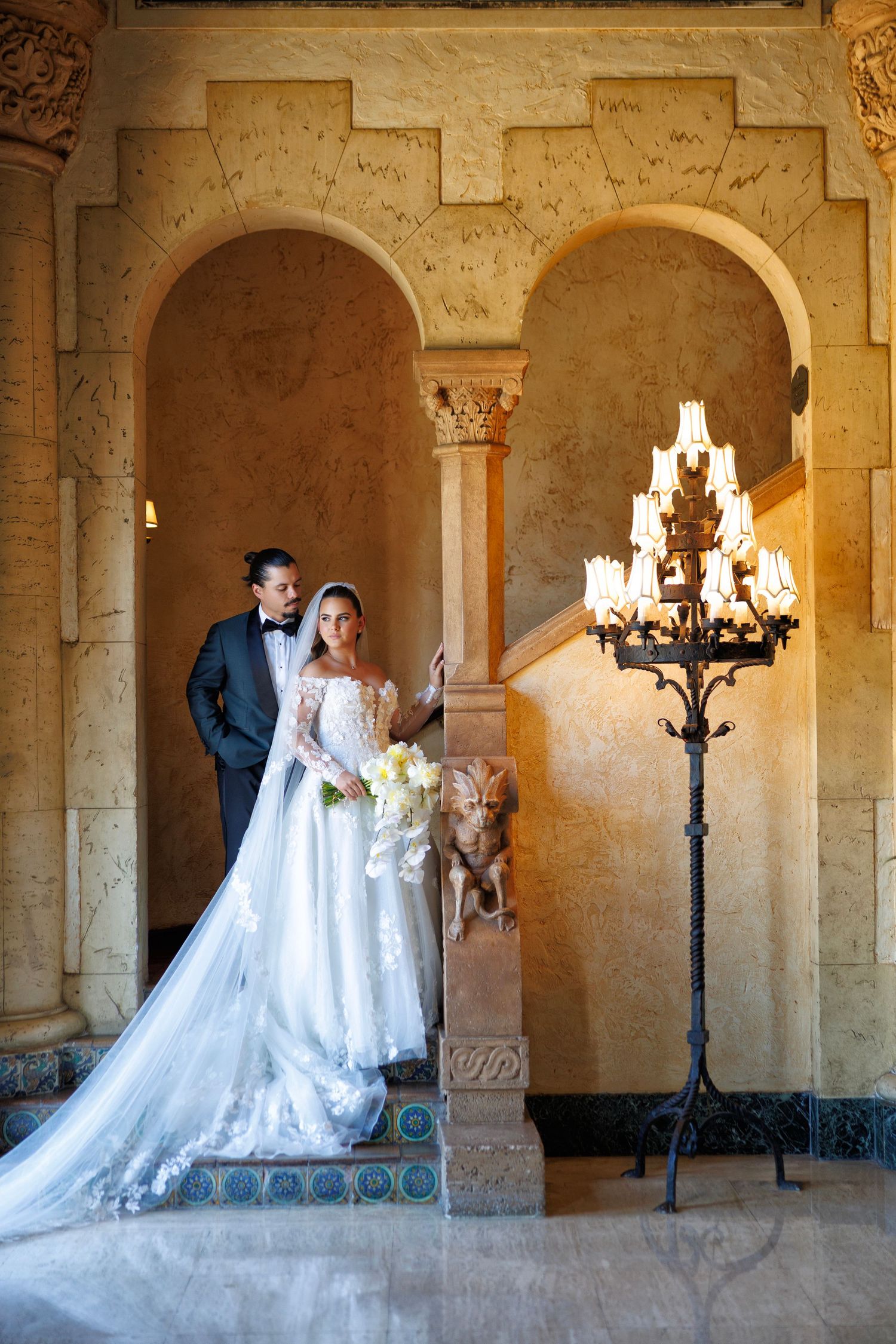 A timeless wedding portrait with the bride and groom posed beneath ornate arches, illuminated by a glowing lantern.