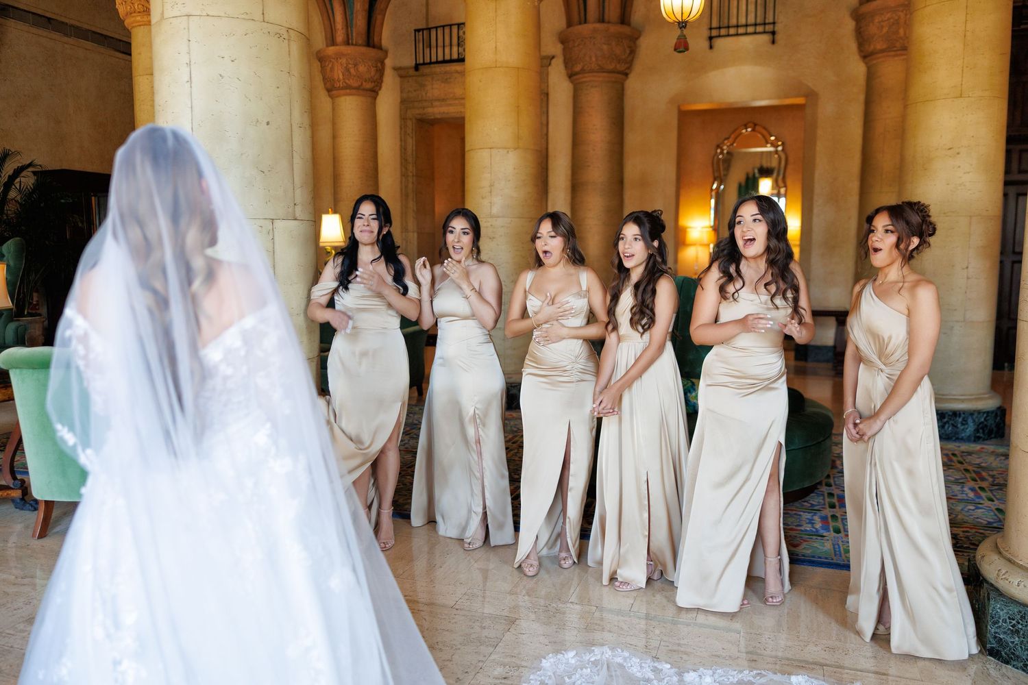 The bride shares a joyful first look with her bridesmaids in elegant gowns.