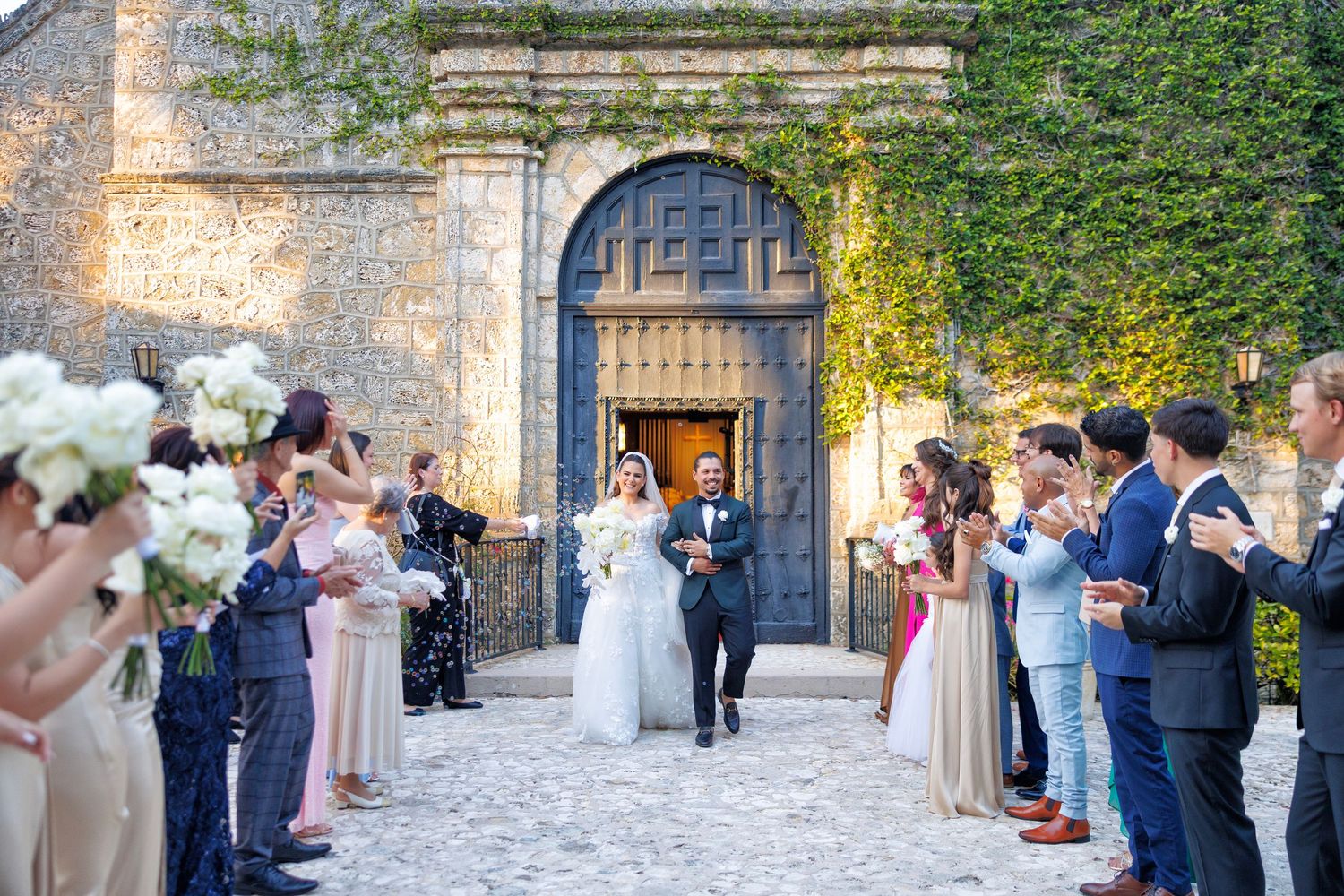 The couple exits the chapel doors as guests cheer with flowers in hand.