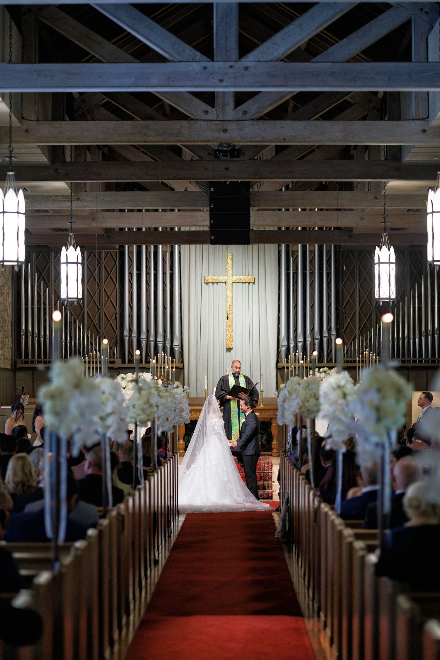 Bride and groom standing at the altar, framed by guests and soft light.