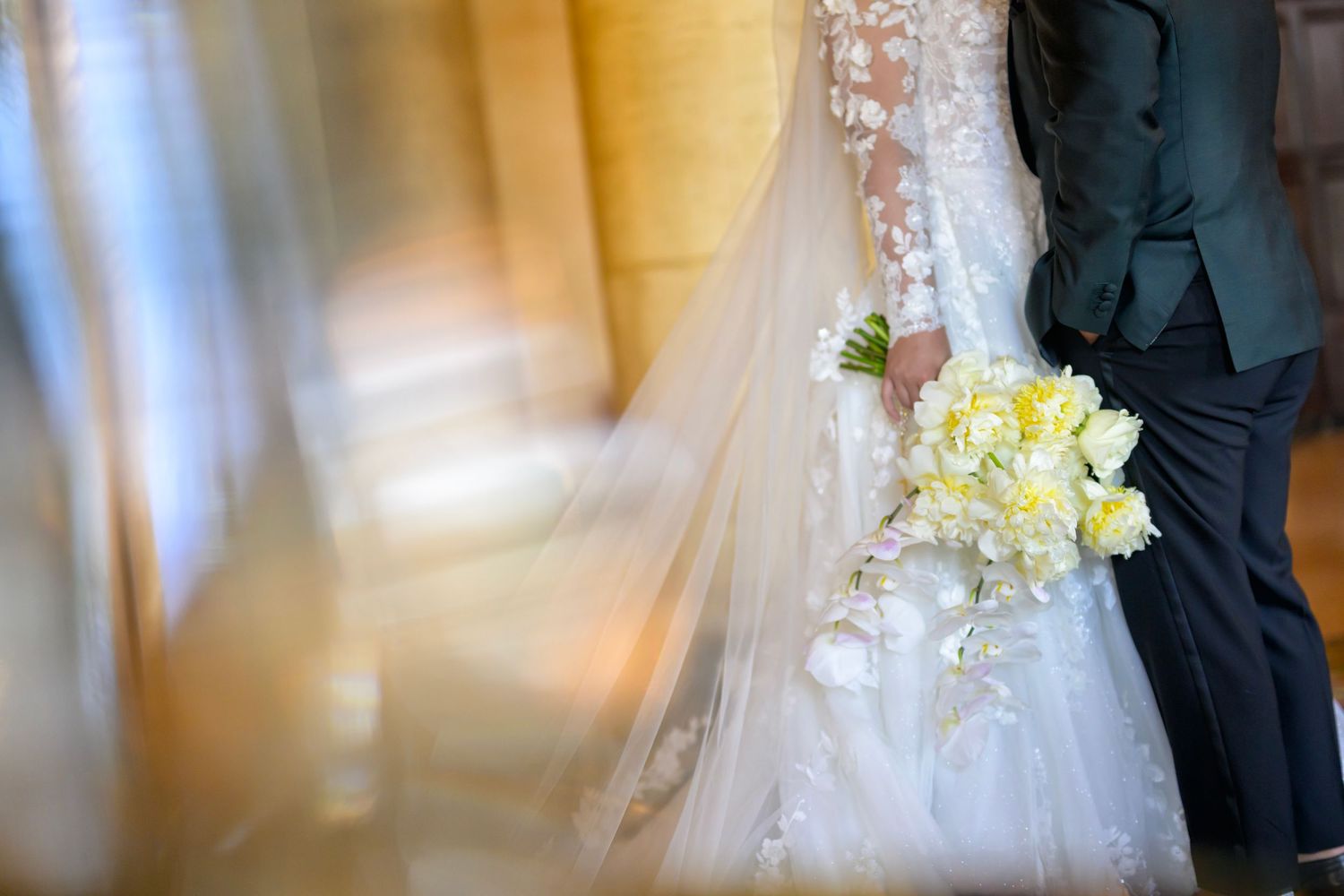 Romantic motion blur of bride’s veil as couple stands with yellow bouquet in hand.”
