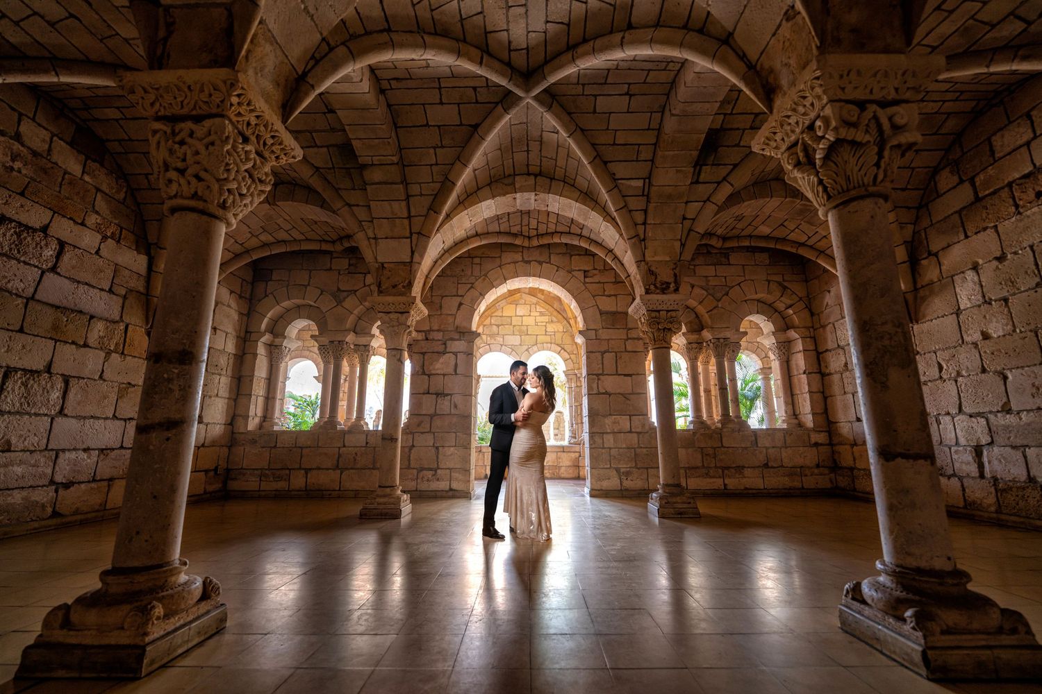Bride and groom portrait framed by historic stone arches—romantic wedding photo with golden light.