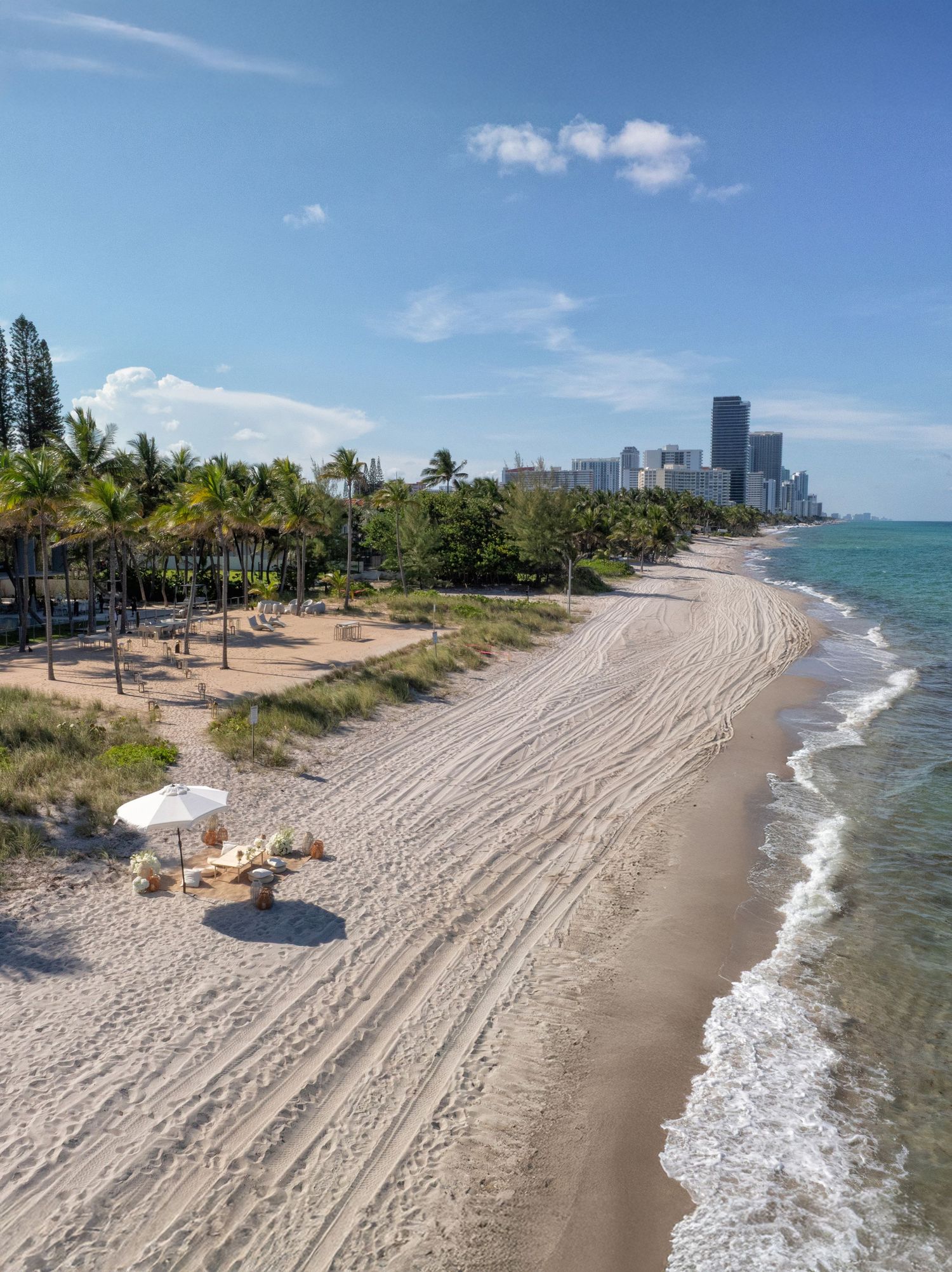 Aerial view of a Miami beach shoreline with turquoise water and city skyline in the distance.