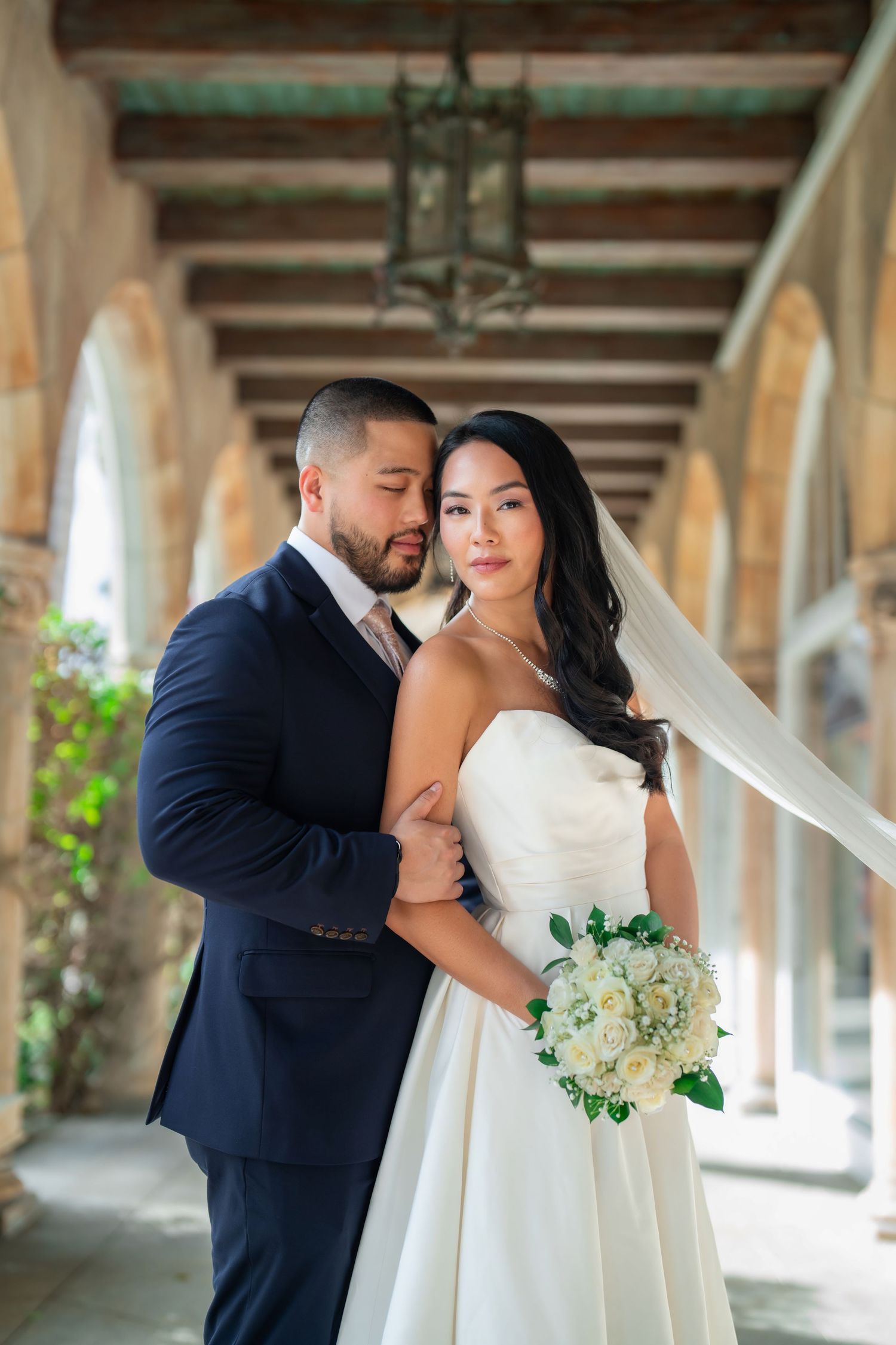 Bride and groom embracing under a covered walkway—refined wedding portrait with natural light.