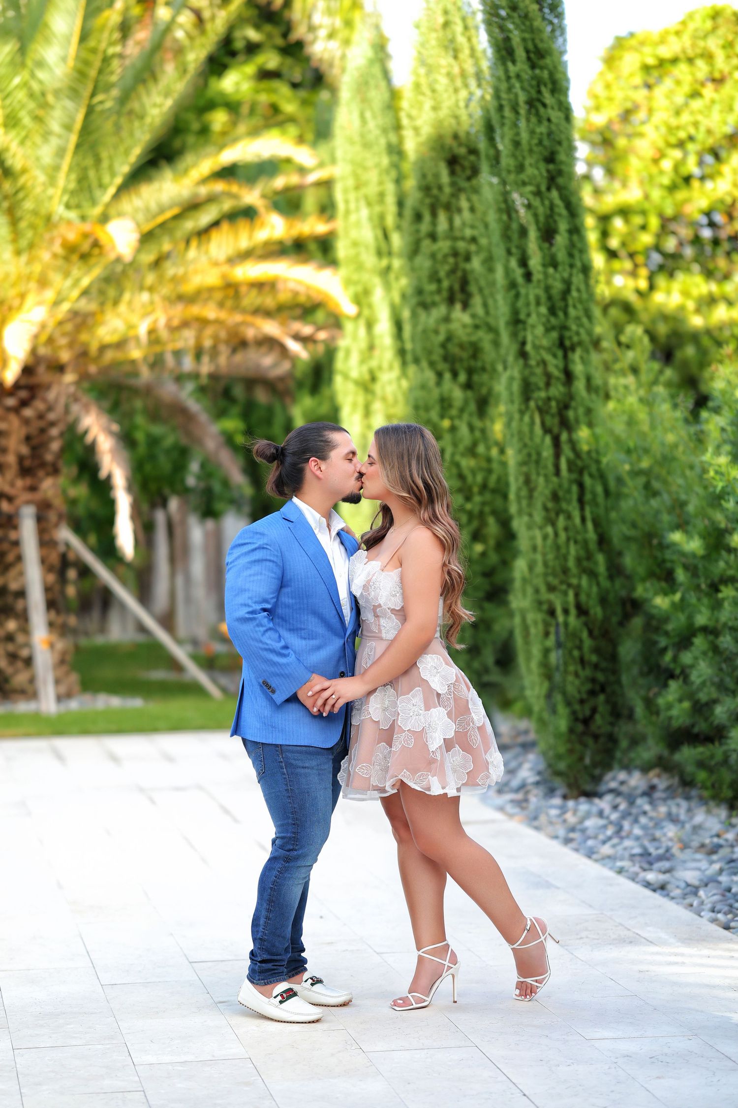 A romantic engagement moment as the couple embraces outdoors, framed by lush greenery and golden light.