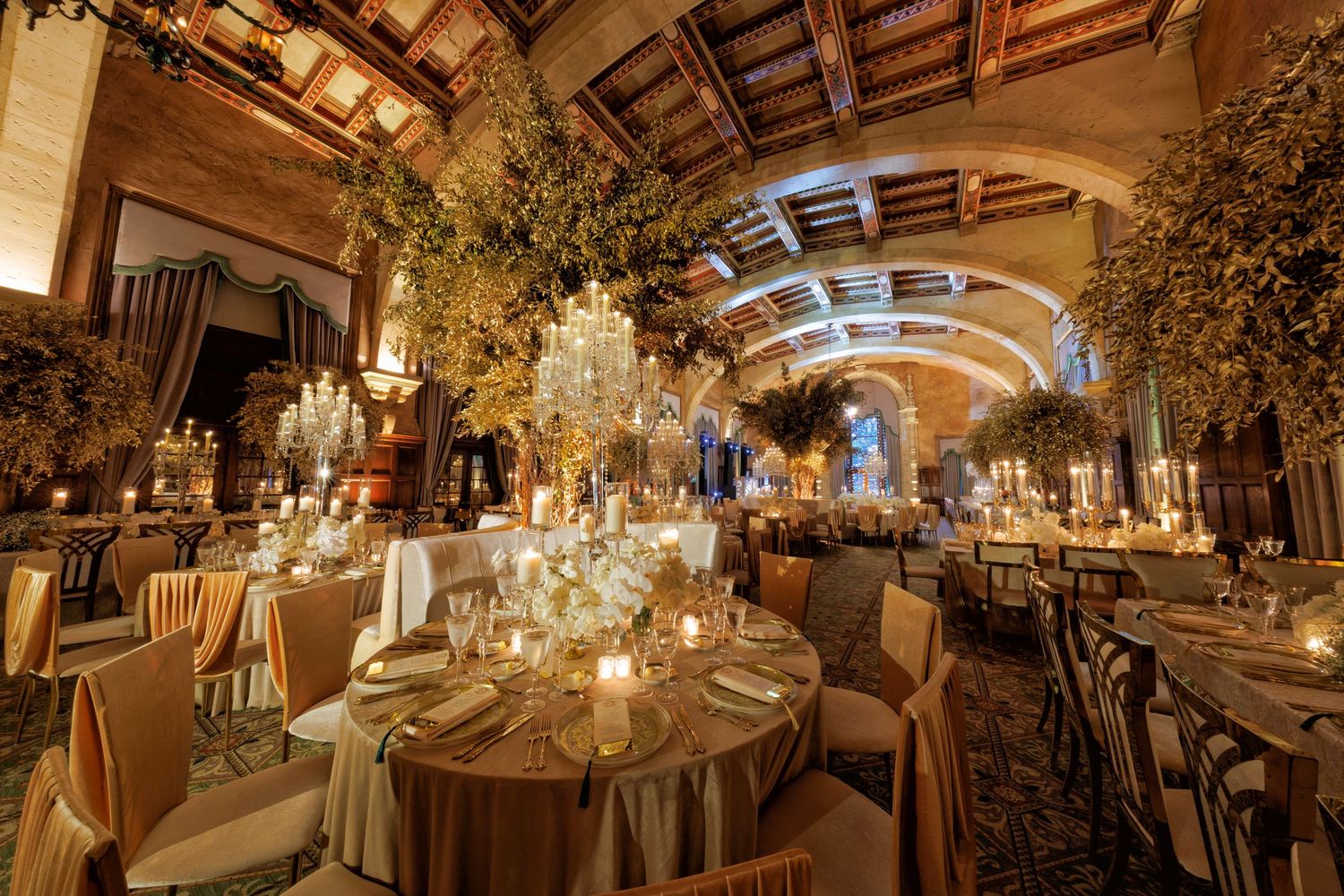 Intimate tables with tall florals, golden glow, and greenery under arches.
