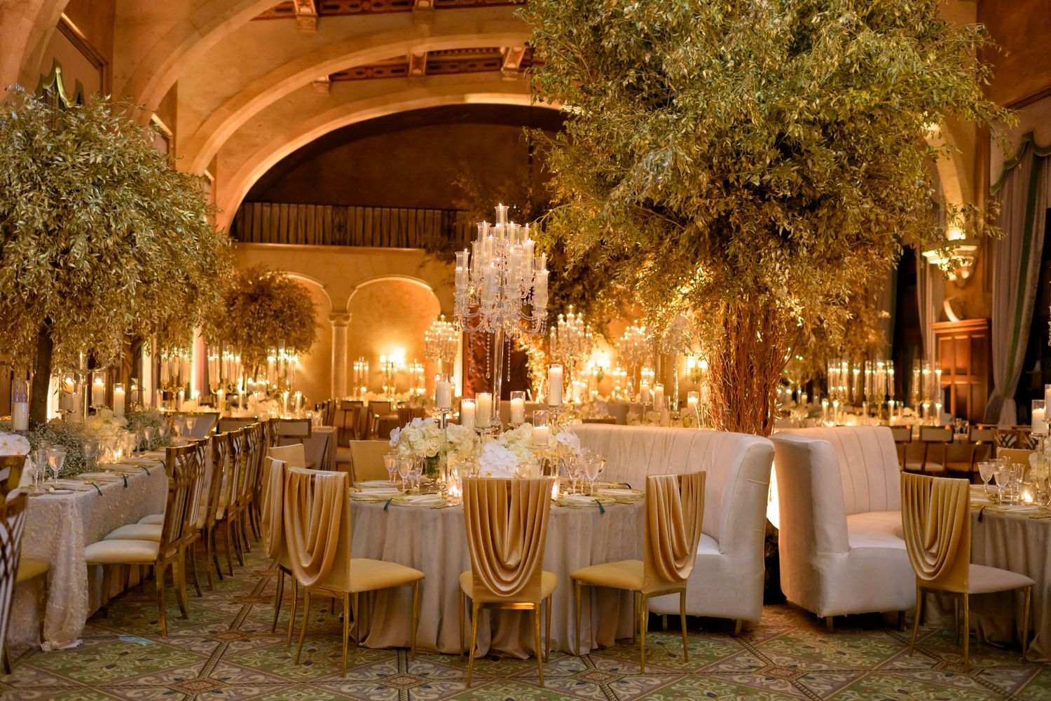 A golden reception hall glows with candlelight and grand floral centerpieces.