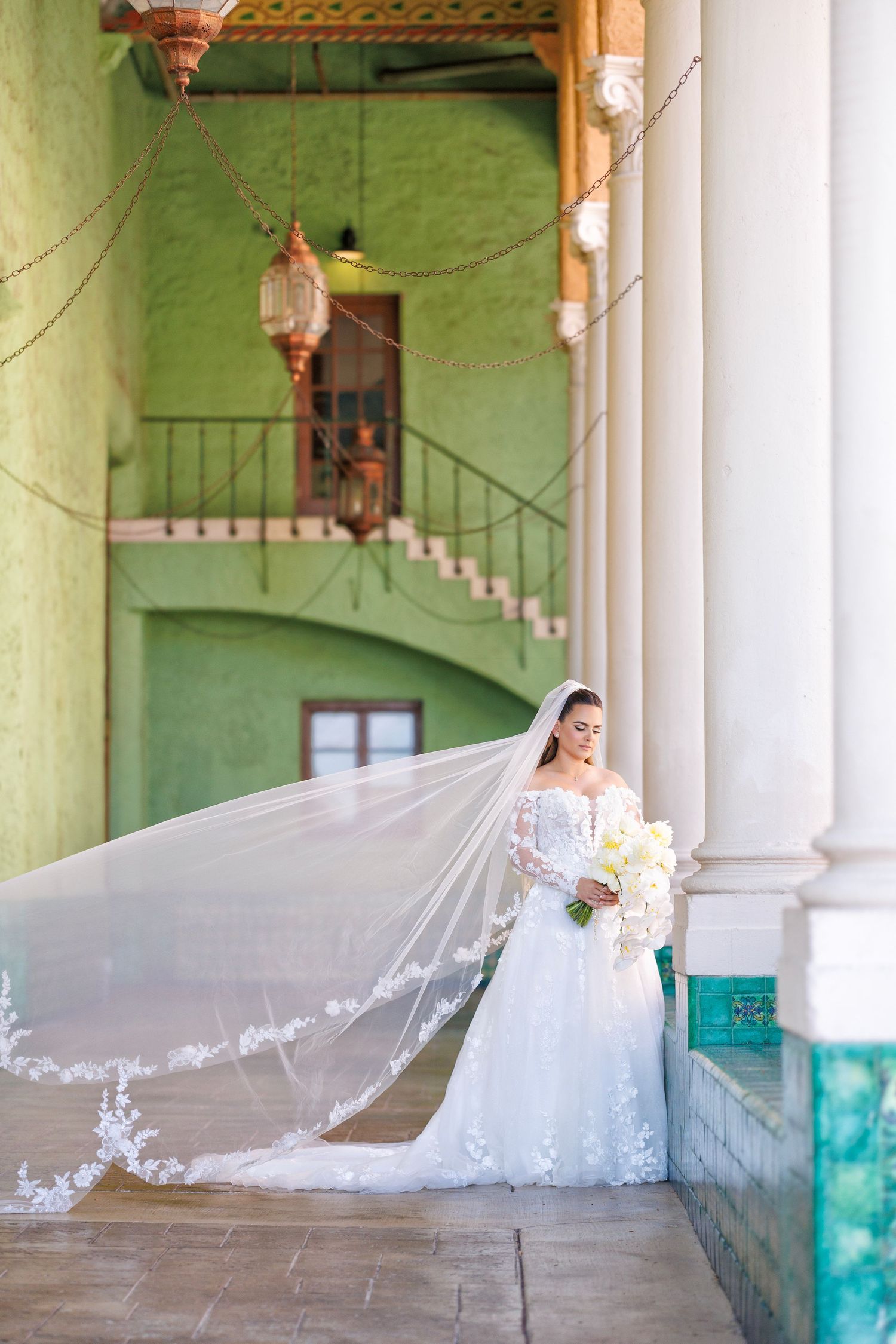 Bride framed in soft light, her long veil cascading against green walls and columns.