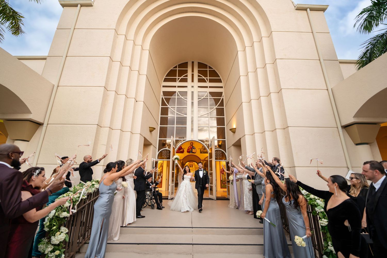 Grand wedding exit outside a cathedral—bride and groom celebrated with guests tossing flower petals.