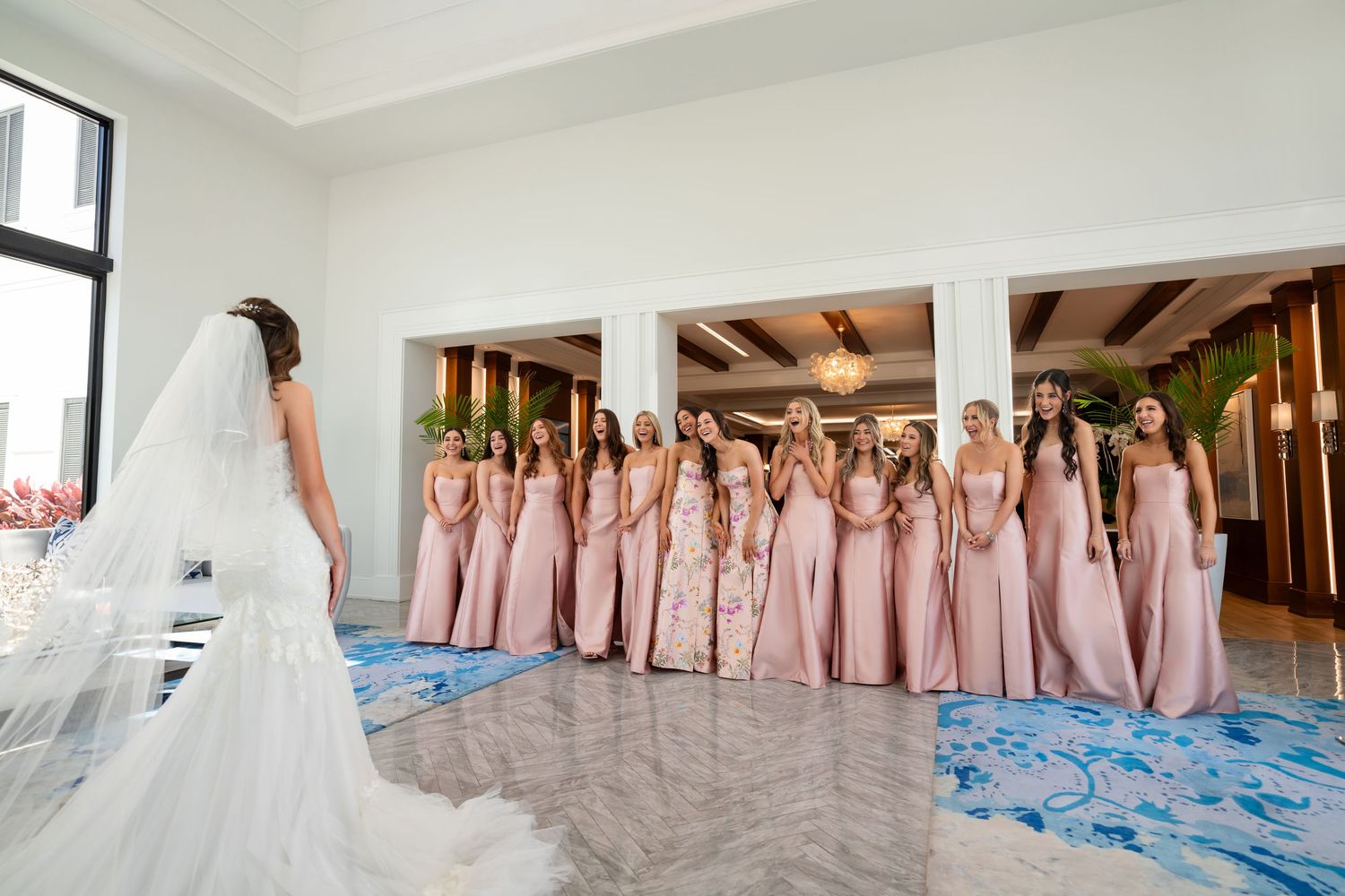 Bride in a white gown standing with bridesmaids dressed in blush pink gowns—elegant bridal party portrait.