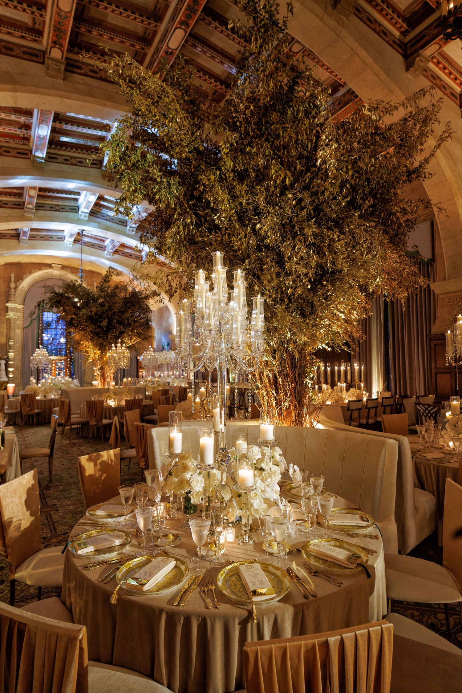Elegant reception table décor featuring tall glass candelabras, lush greenery, and warm golden lighting.