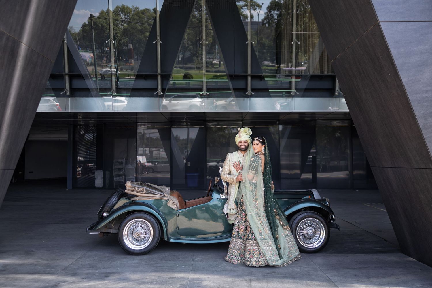 Couple posing beside a vintage car outside a modern Mexico City venue, blending tradition with cinematic style.