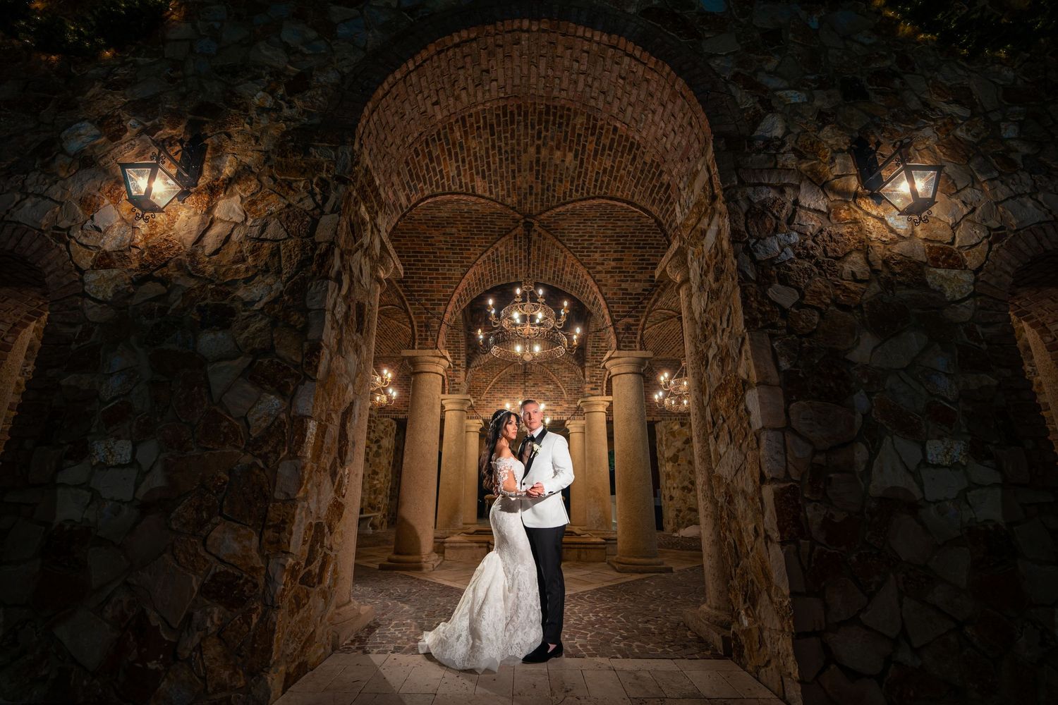 Bride framed in a dramatic stone archway—cinematic wedding portrait with warm golden light.