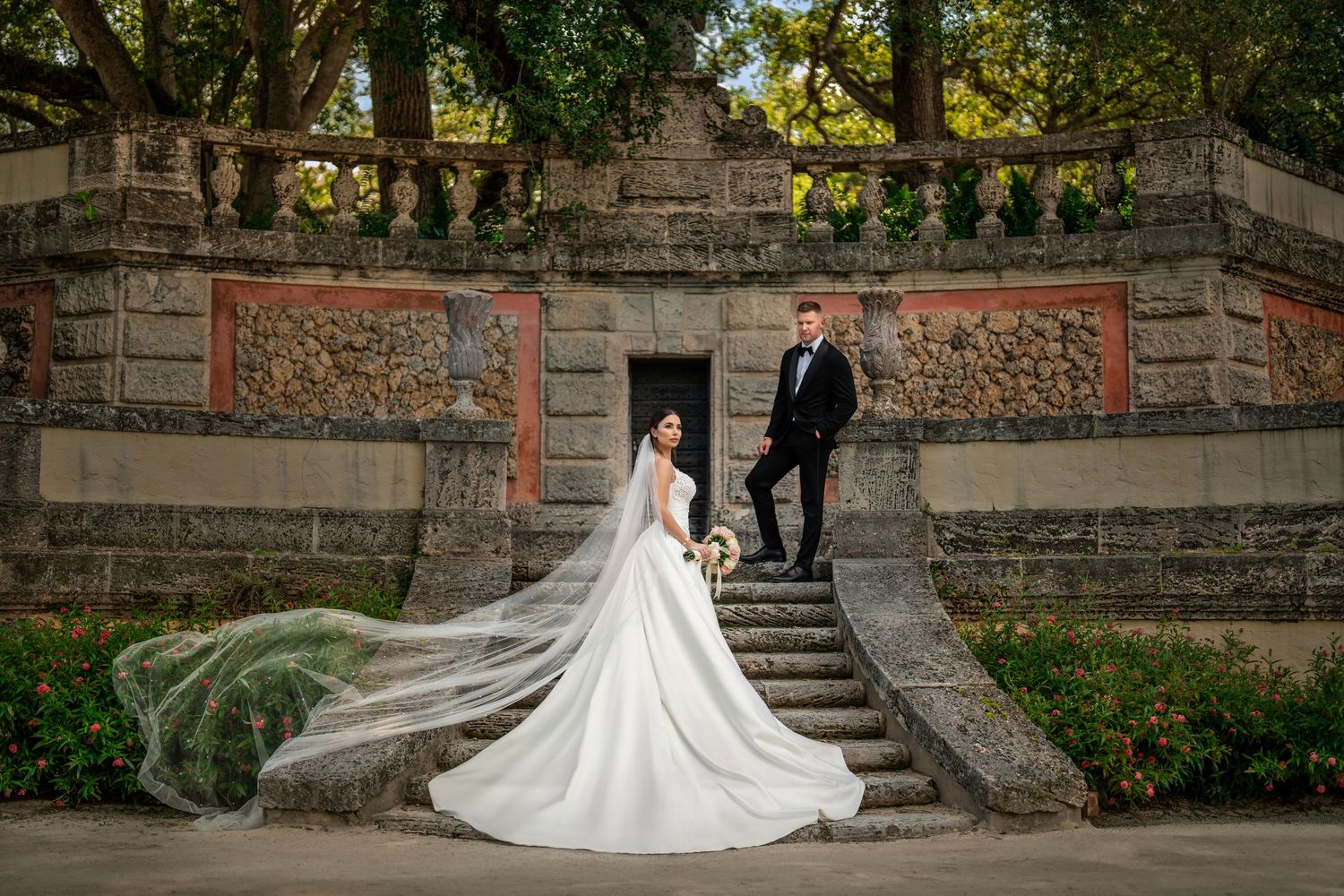 Bride and groom walking down stone steps surrounded by lush greenery—romantic outdoor wedding portrait.