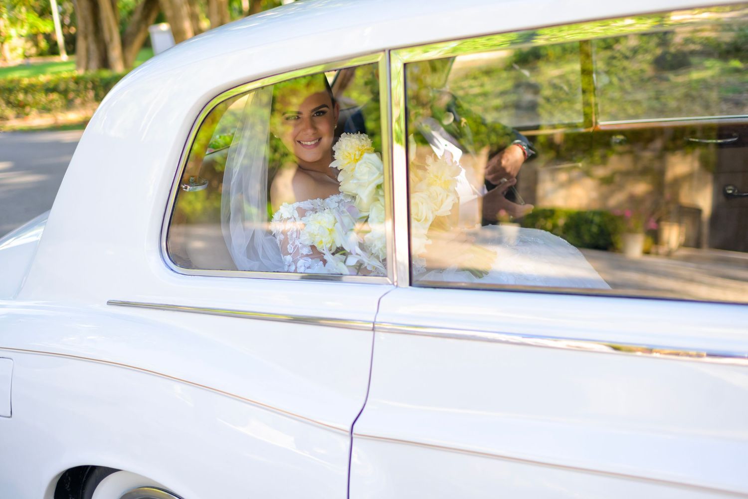Bride looks radiant through the window of a vintage white car.