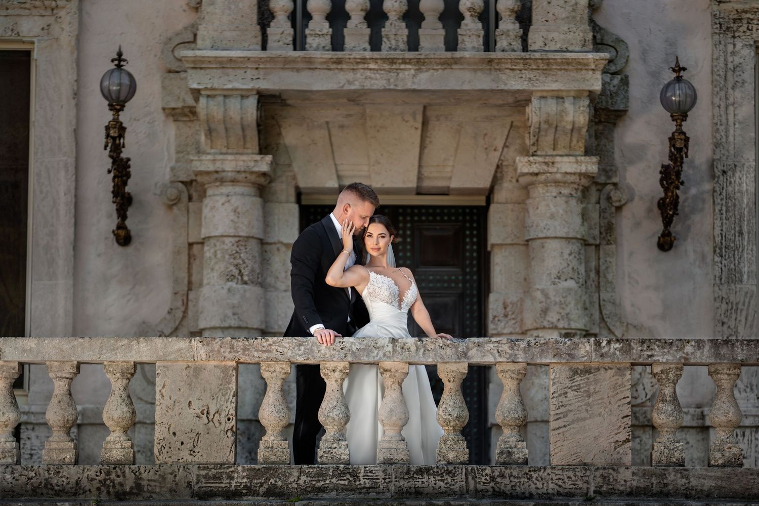 Bride and groom seated on a stone balcony at a historic venue—romantic editorial wedding portrait.