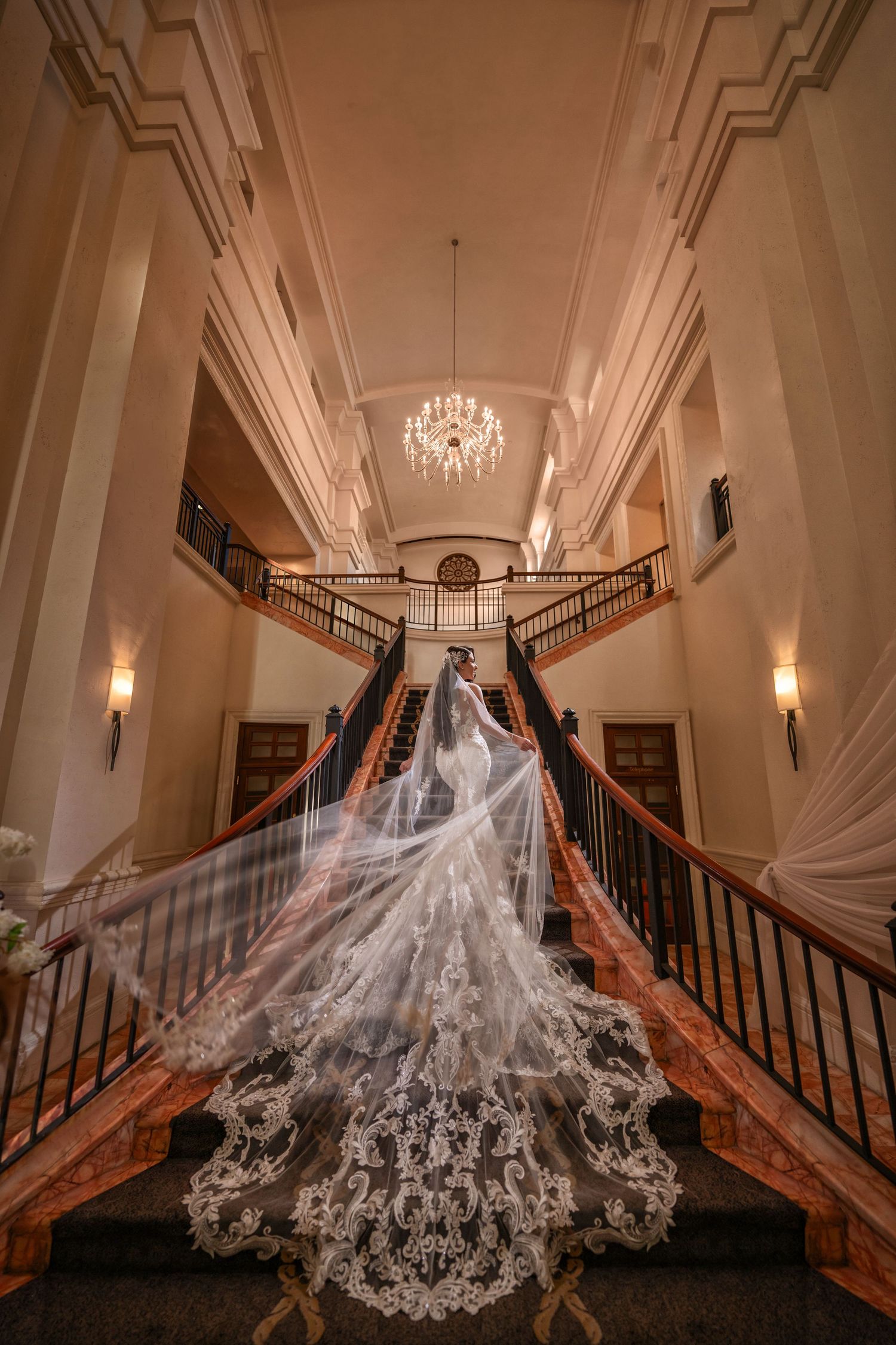 Bride in a couture gown descending a dramatic staircase—luxury wedding detail with cathedral train.