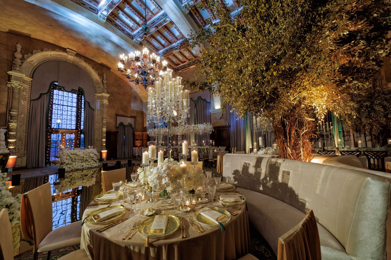 Reception tables beneath a skylit ceiling, framed by greenery and golden light.