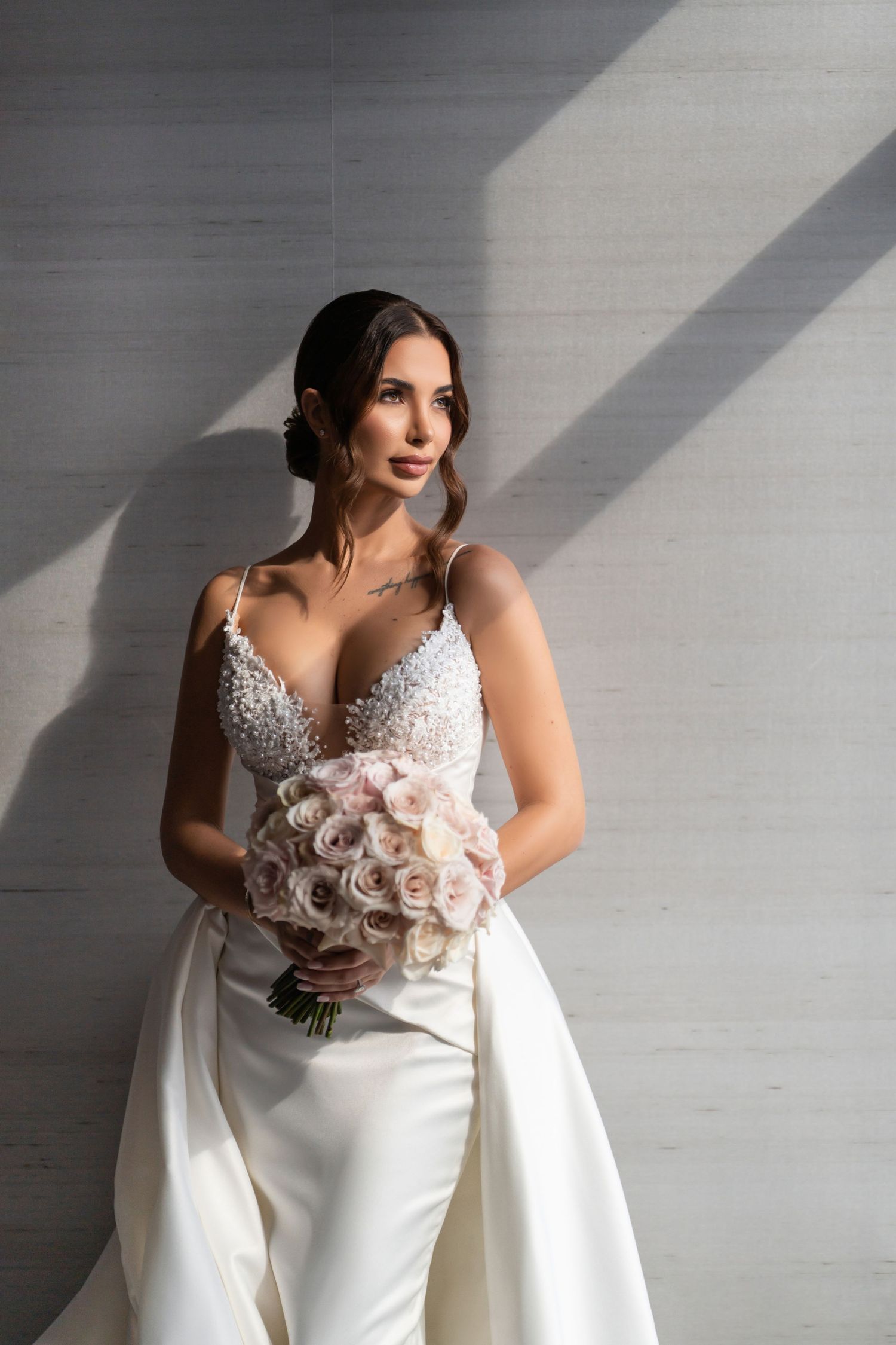 Bridal portrait with natural window light—bride holding bouquet in an elegant white gown.