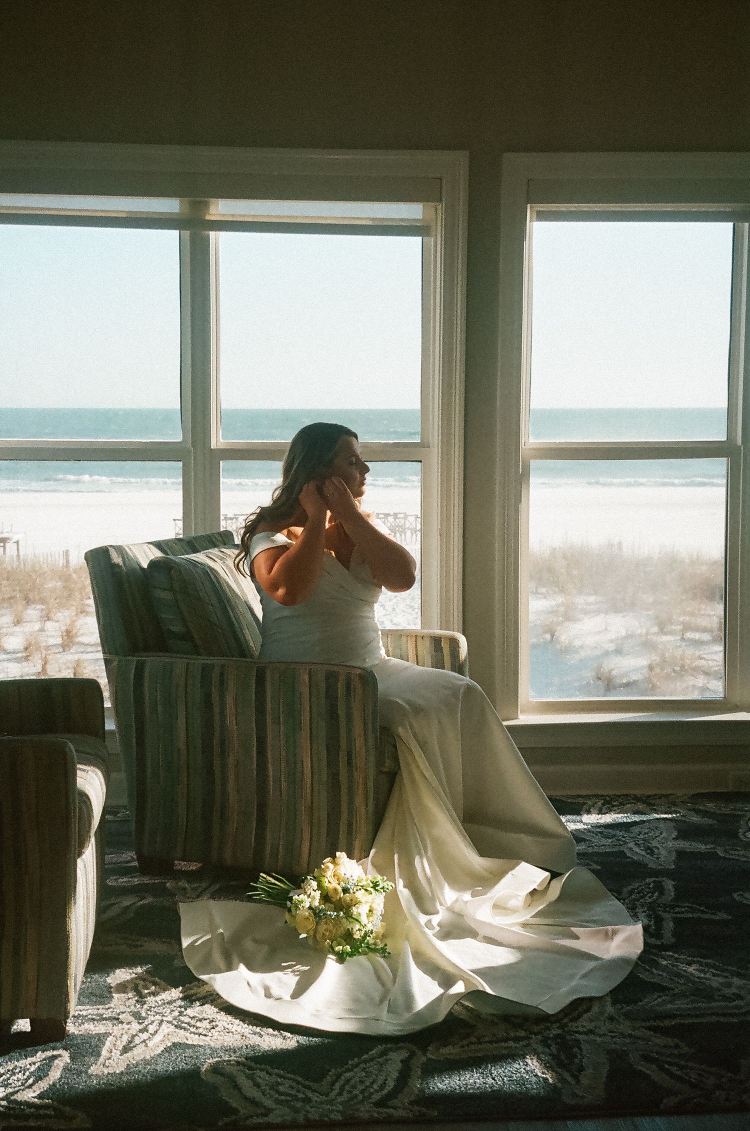 Bride adjusting her earring in front of a window during a beach micro wedding in Alabama