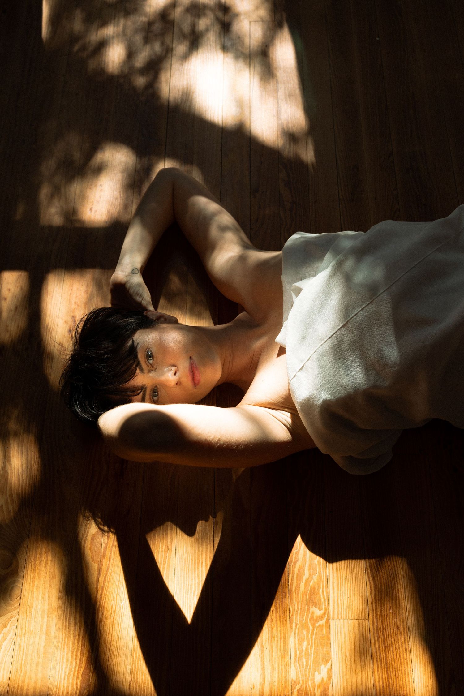 Fine art portrait of a woman lying beneath a sheet with window light