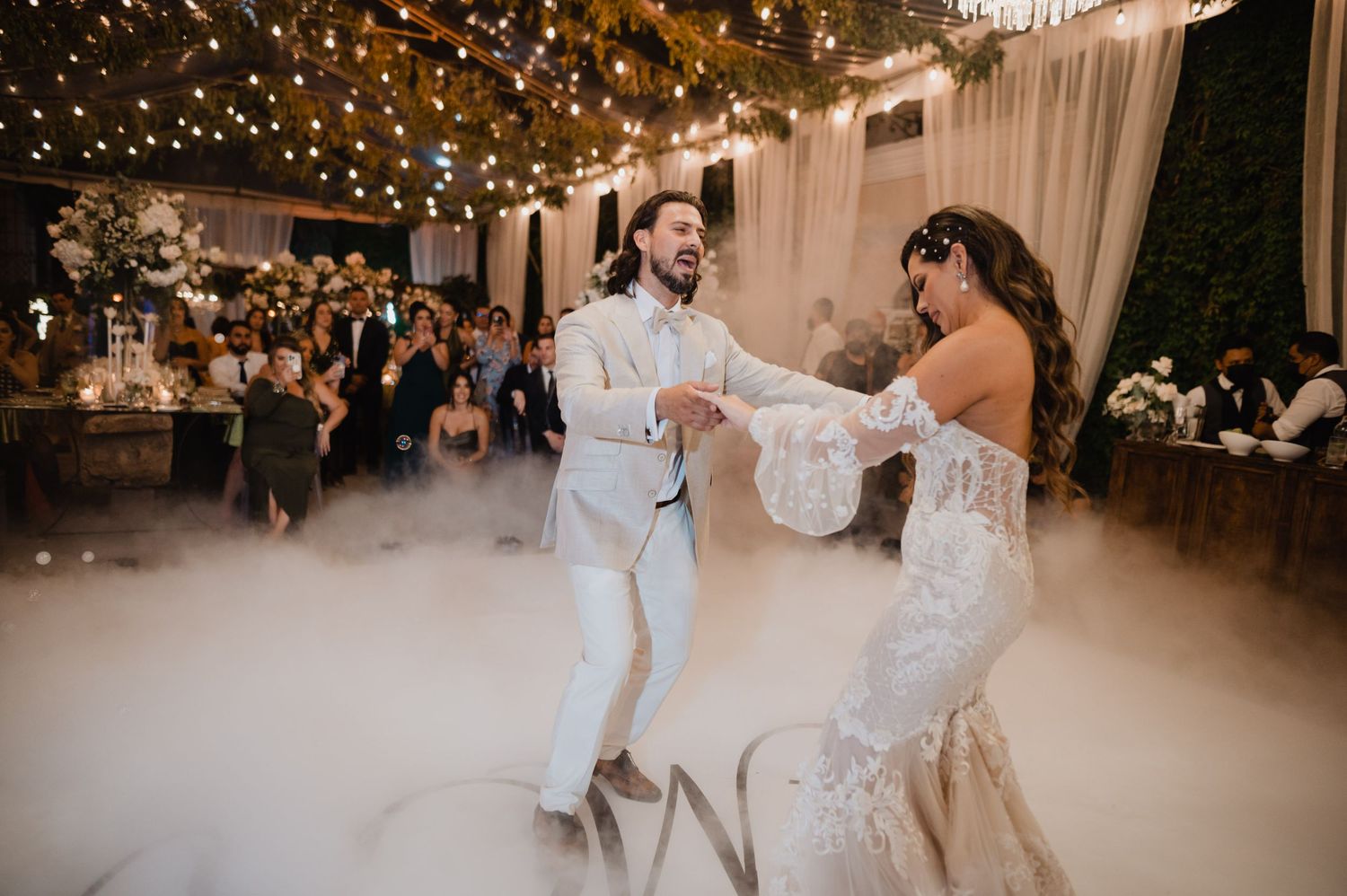 Newlyweds dancing under twinkling lights at an elegant indoor reception with fog effects.