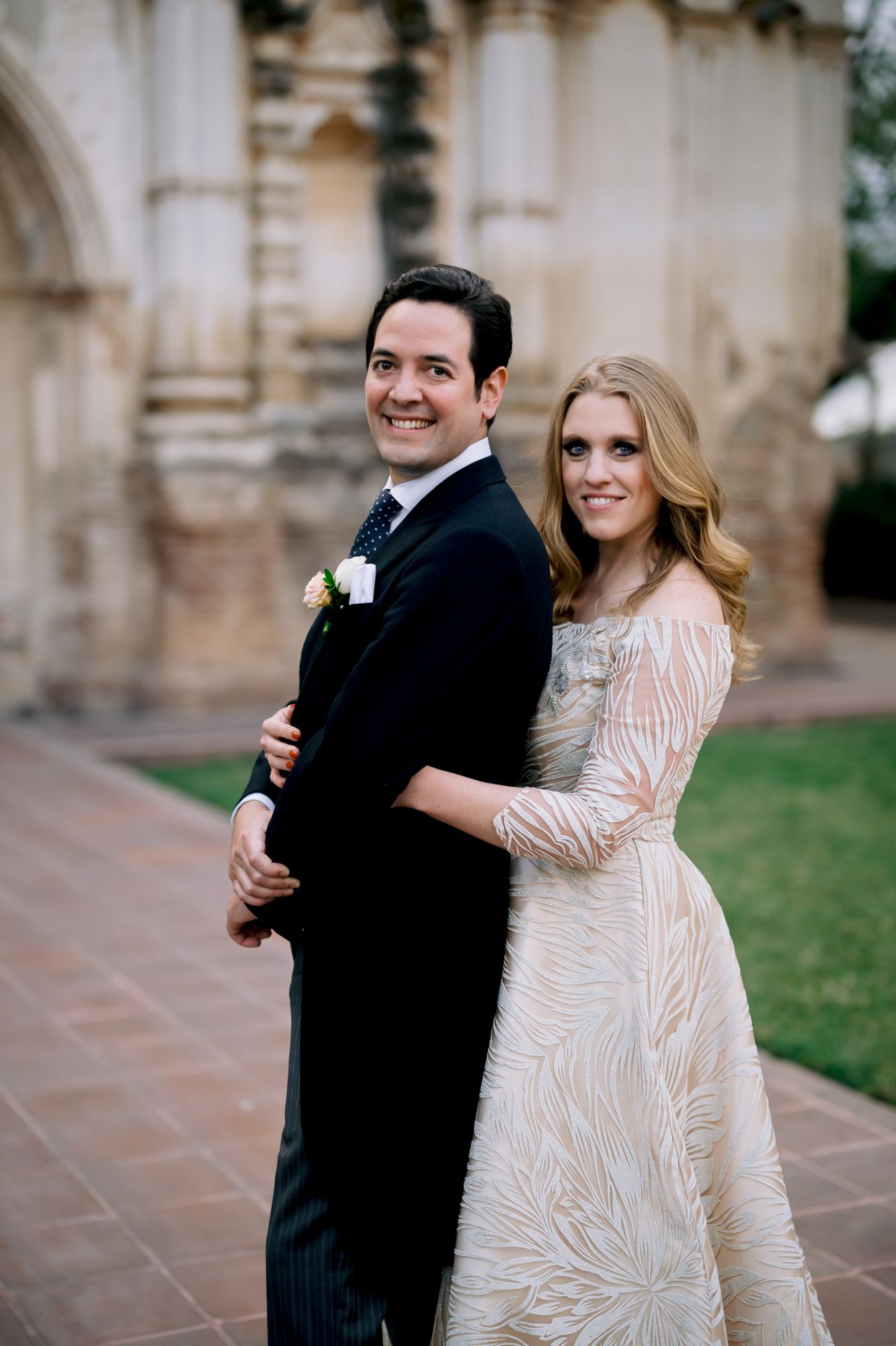 A romantic wedding portrait of a couple in formal attire posing outside a historic building.