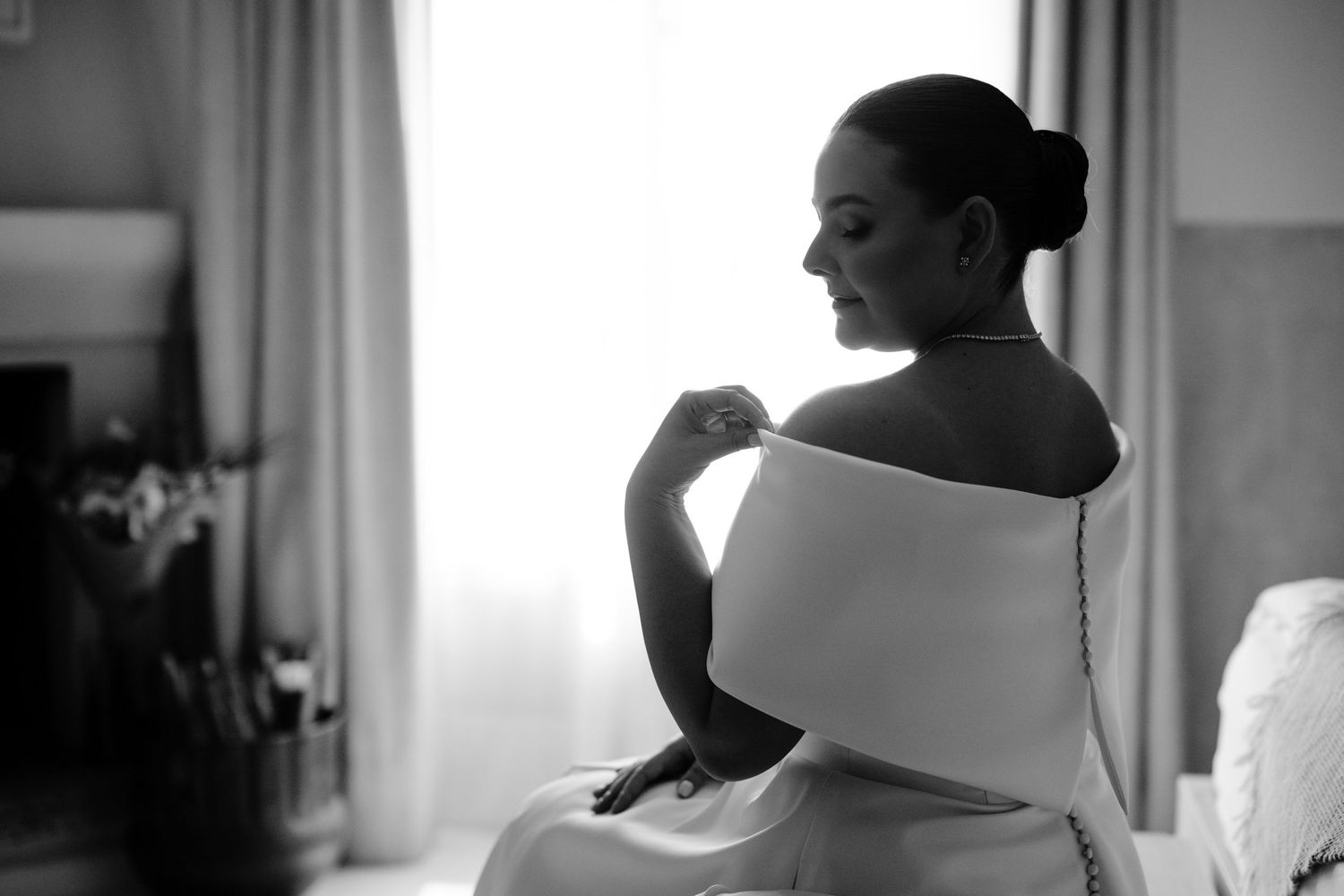Black and white portrait in natural window light showing elegant bridal silhouette.