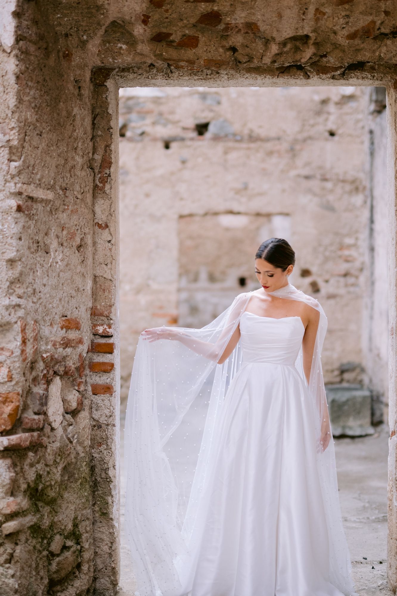 Elegant white wedding dress with flowing cape sleeves photographed in rustic stone doorway.