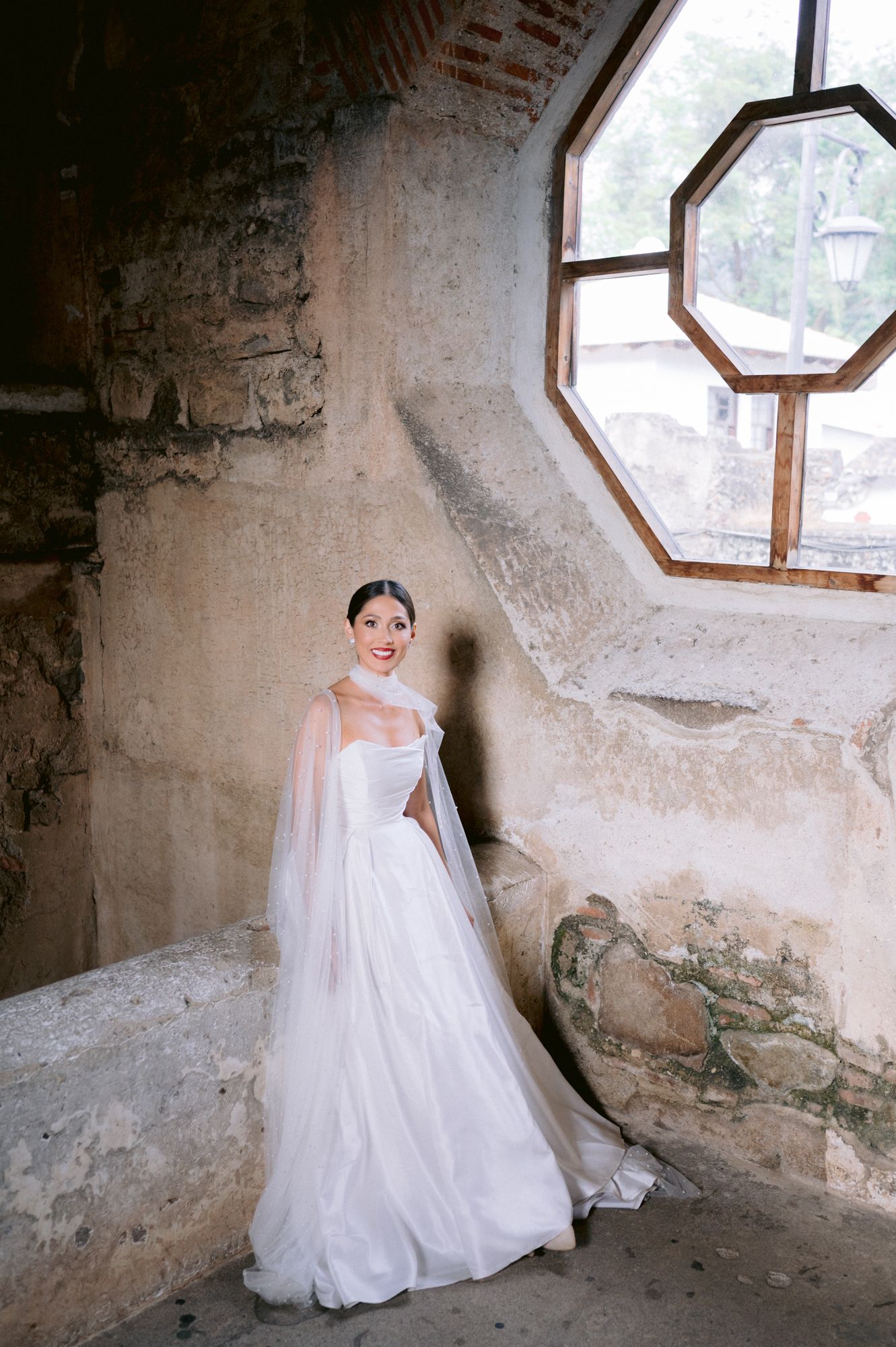 A wedding dress photographed in a rustic stone room with an octagonal window.