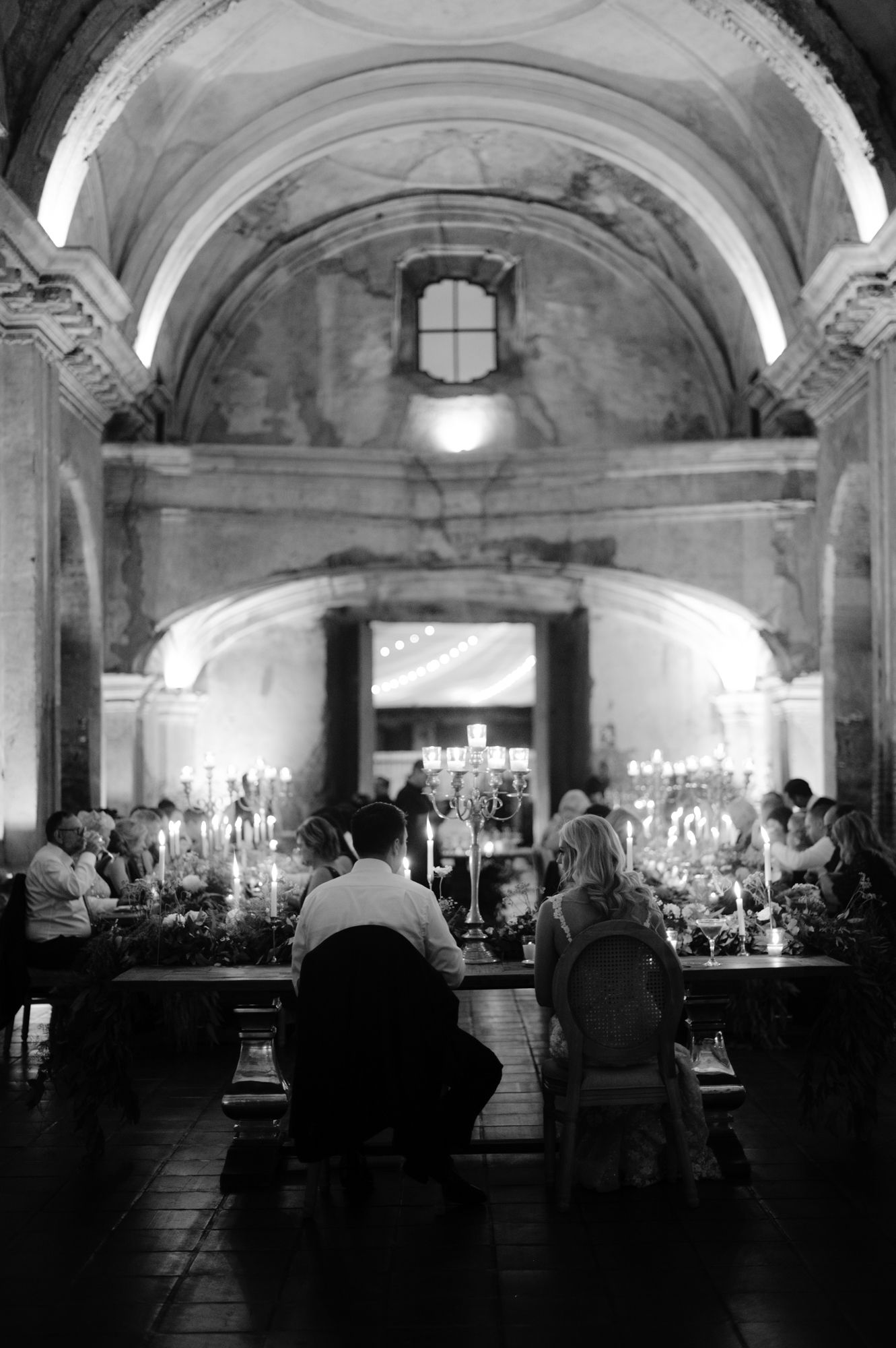 Wedding reception dinner setup in historic stone venue with vaulted ceilings and candlelight.