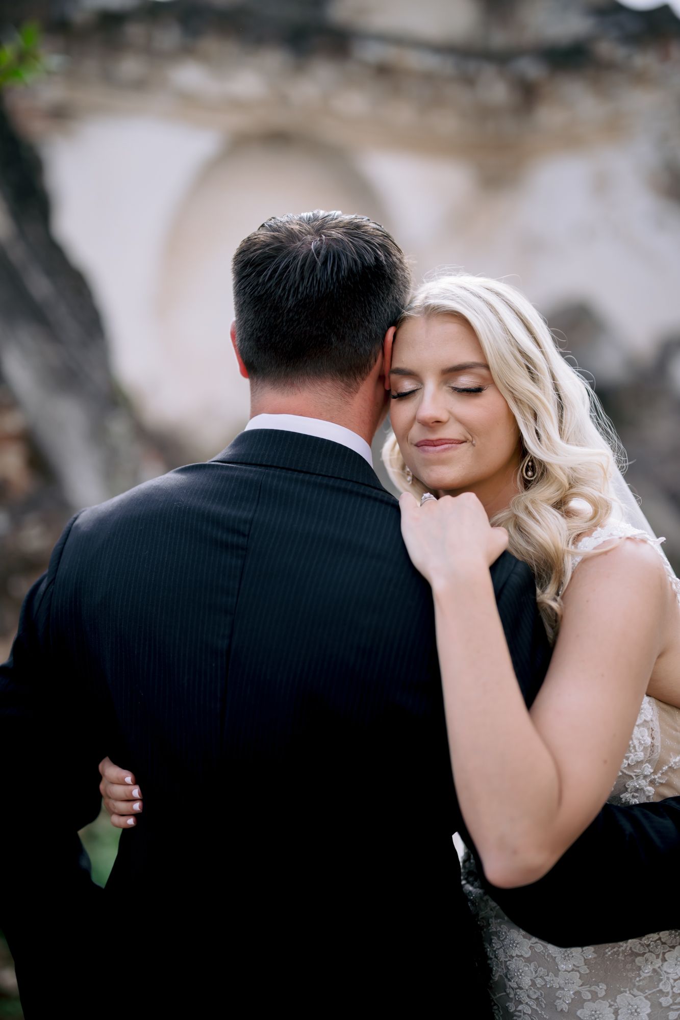 An intimate embrace between newlyweds with the bride in a lace gown against stone archways.
