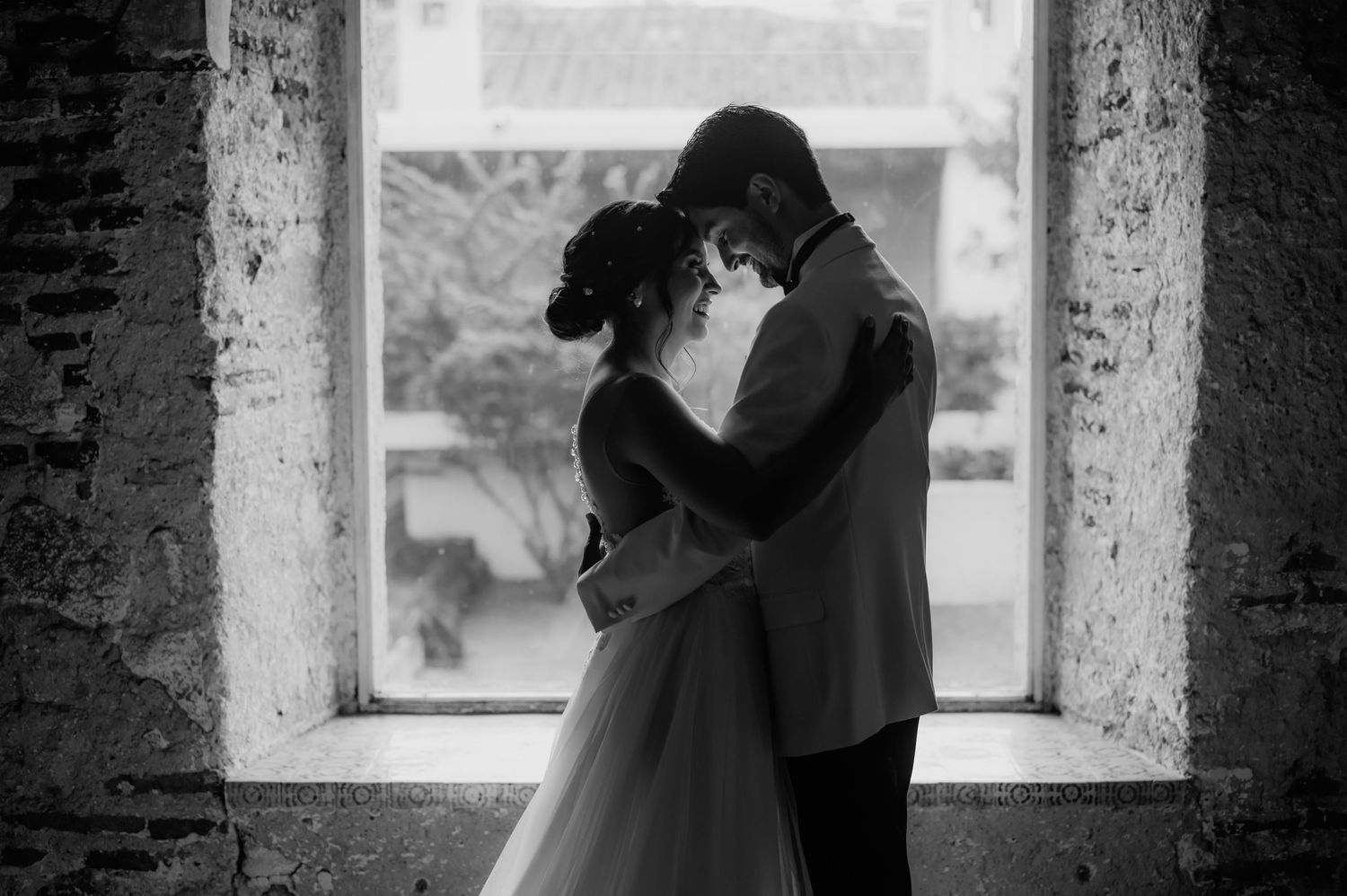 Silhouetted couple embraces in window frame of historic stone building.