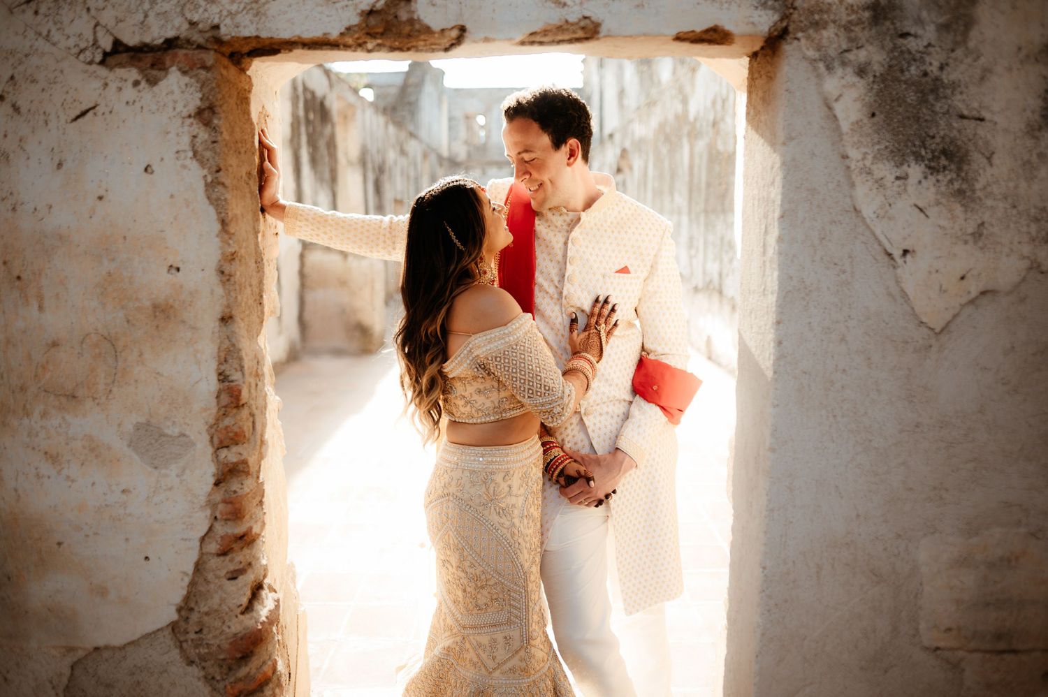 Couple shares intimate moment in sun-lit doorway of rustic stone building.
