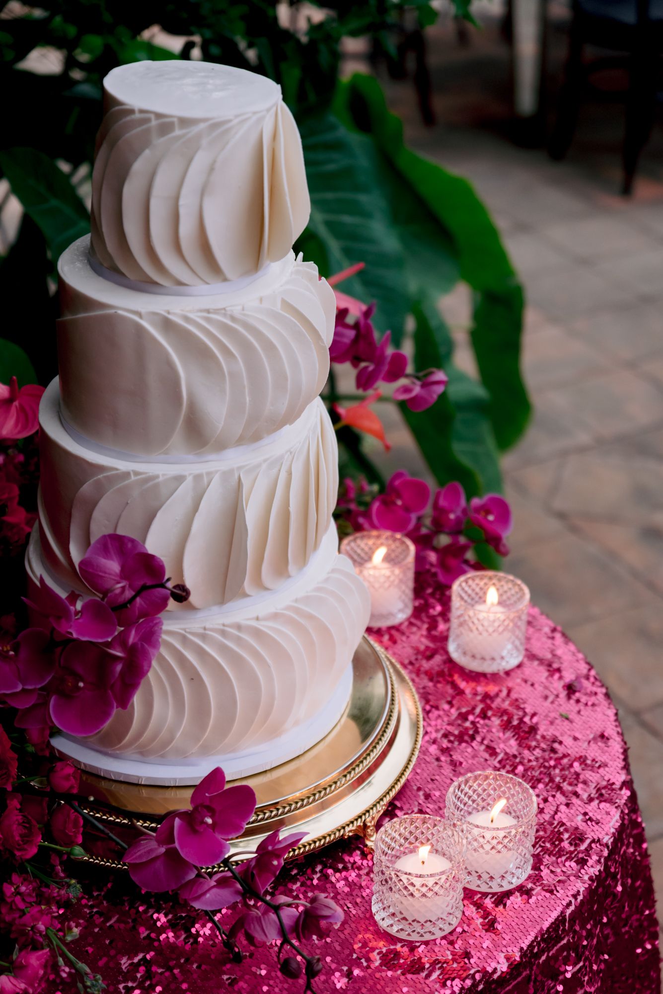 Modern white wedding cake with pleated texture and fuchsia orchids on sparkly pink tablecloth.