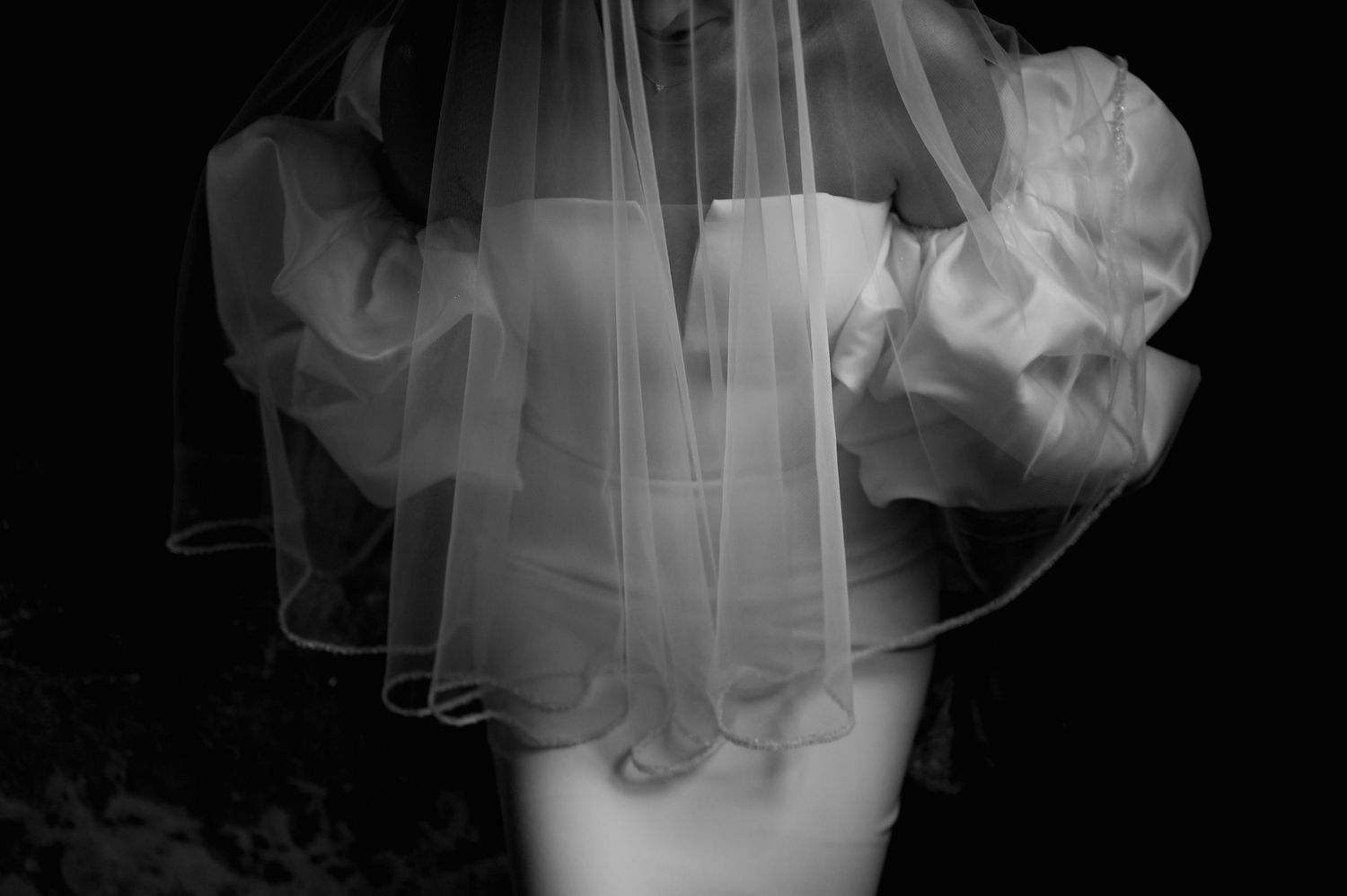Artistic black and white capture of billowing bridal veil creating ethereal movement against dark backdrop.